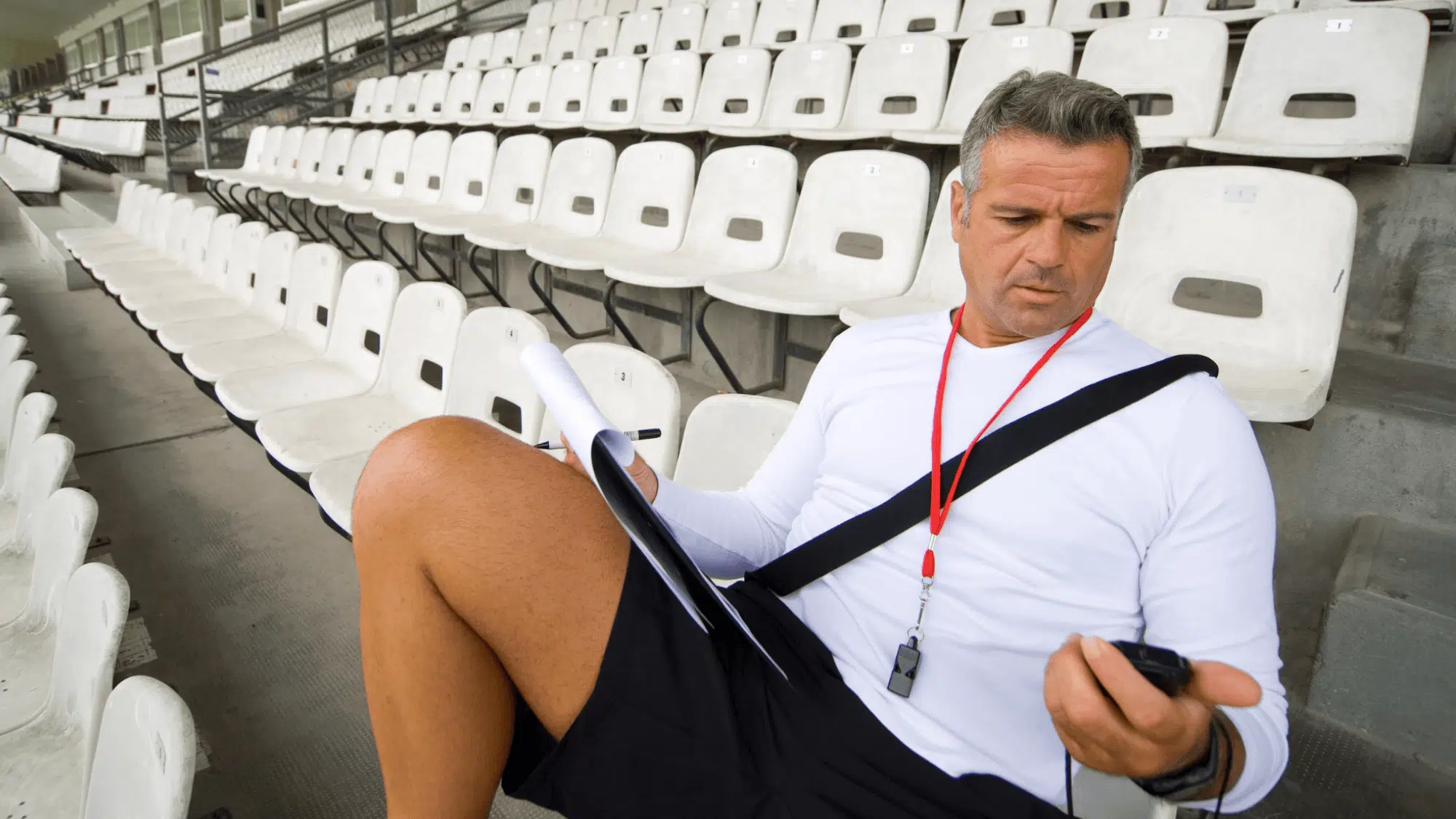 a coach noting down timing of his team to know their current status while sitting on stadium bench