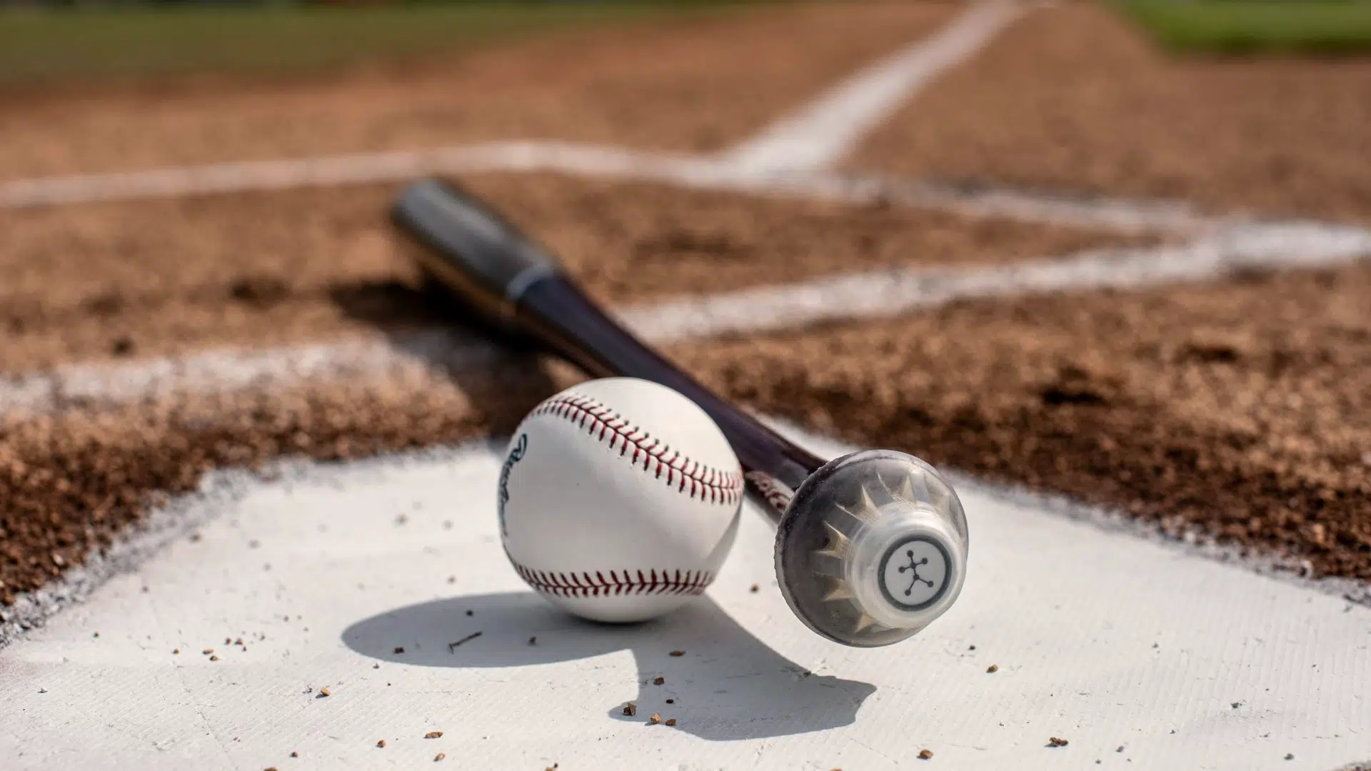 a baseball and bat resting on home plate on a dirt field capturing blast motion baseball energy before a game