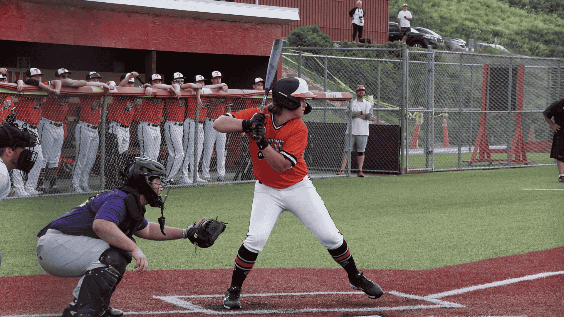 a baseball batter in an orange jersey stands ready at the plate while a catcher waits behind him