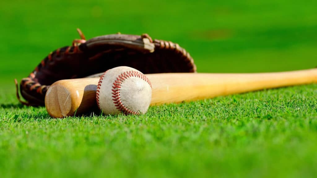 a baseball lies on the grass beside bat and gloves