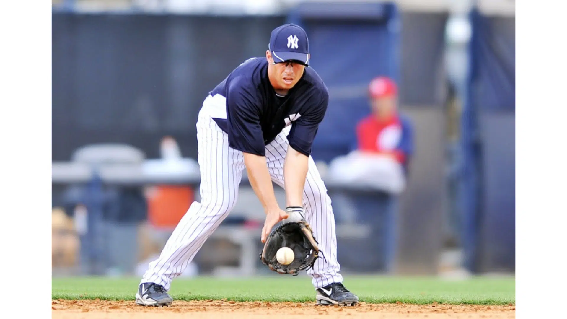 a baseball player in a navy jersey and pinstriped pants fielding a ground ball with his glove on a dirt infield