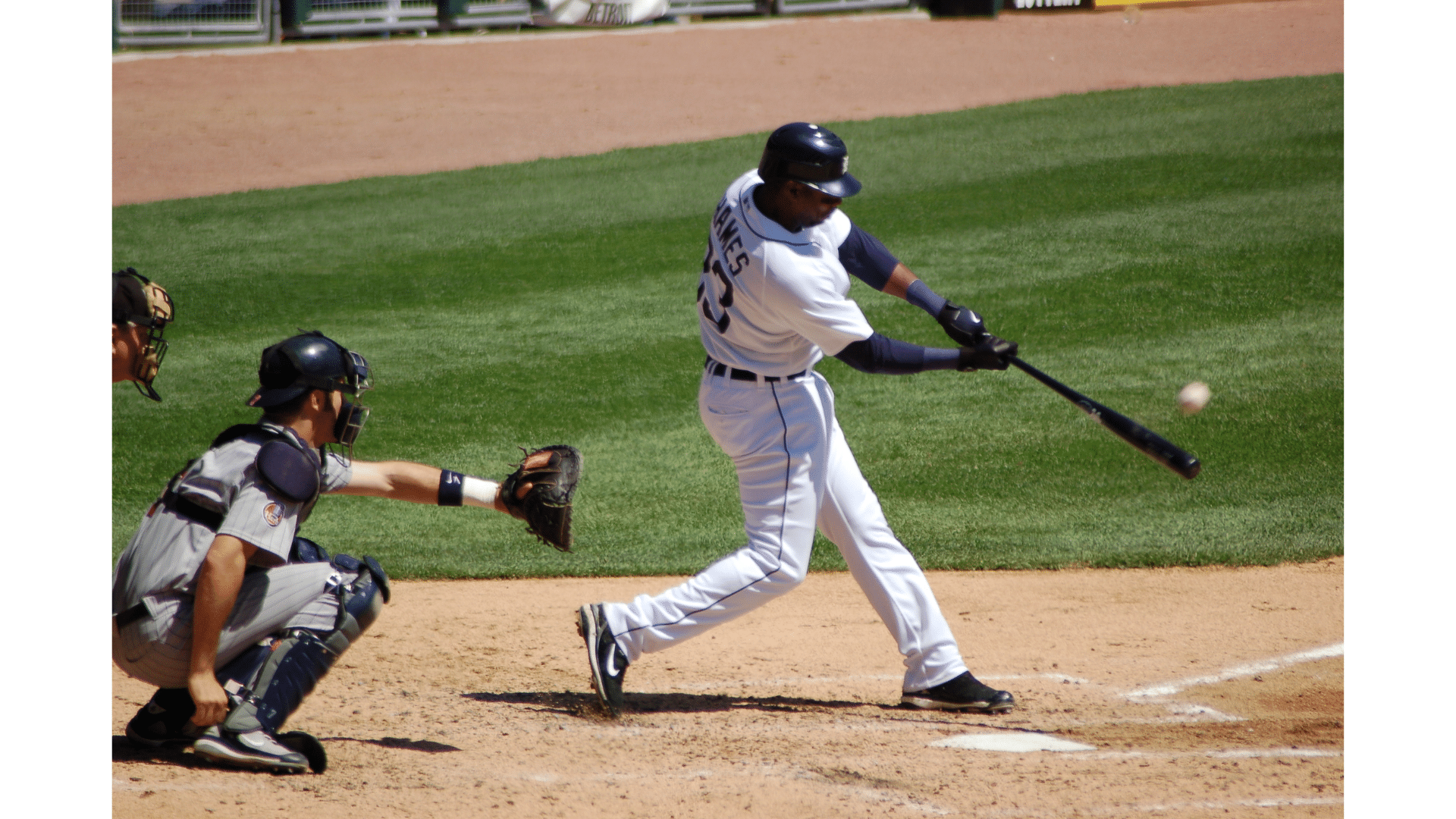 a baseball player in a white uniform swinging a bat at a pitch while a catcher crouches behind home plate on a sunny field