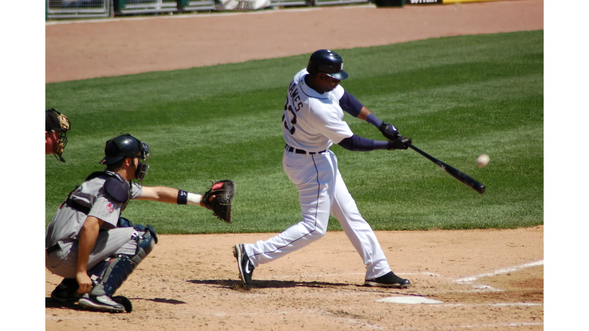 a baseball player in a white uniform swinging a bat at a pitch while a catcher crouches behind home plate on a sunny field