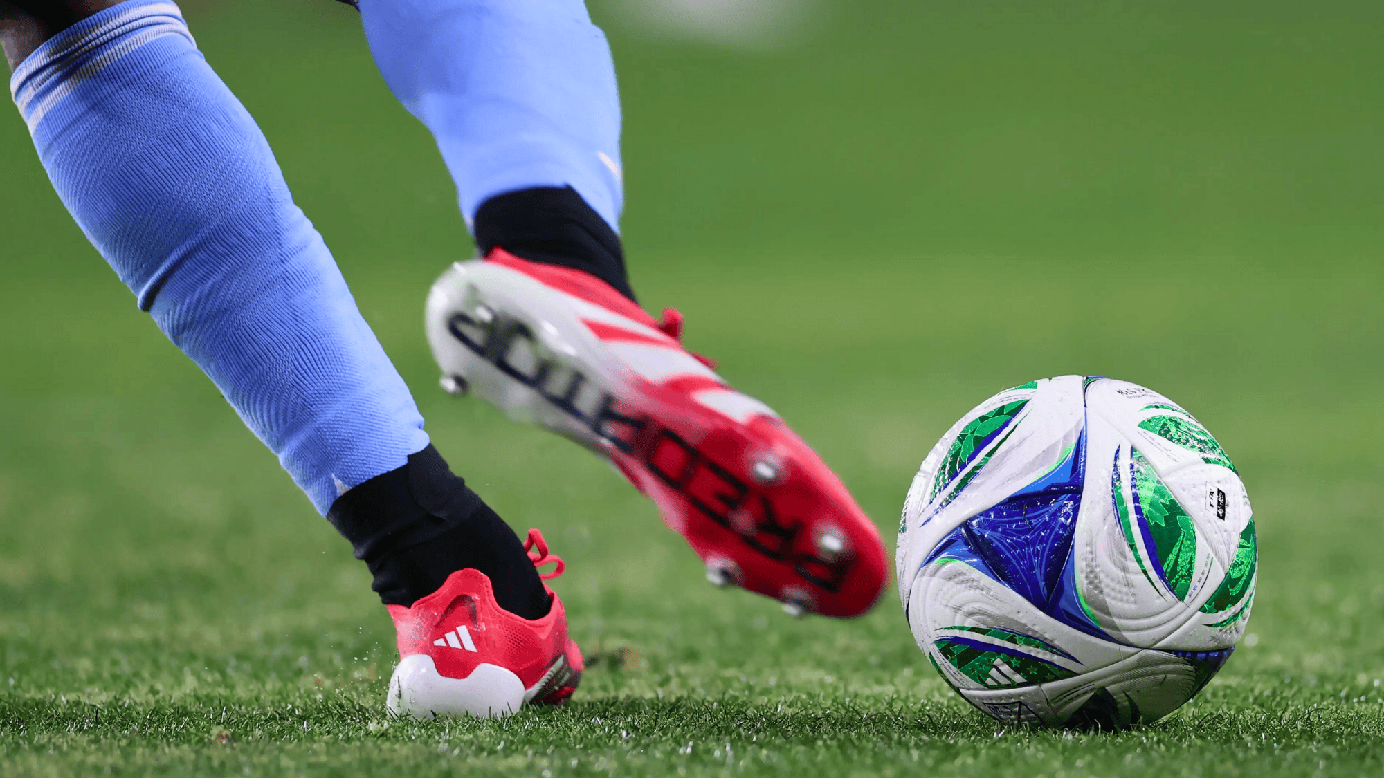 a-centre-back-soccer-player-wearing-red-cleats-kicking-a-ball-on-a-green-field-during-a-match-on-grass-pitch