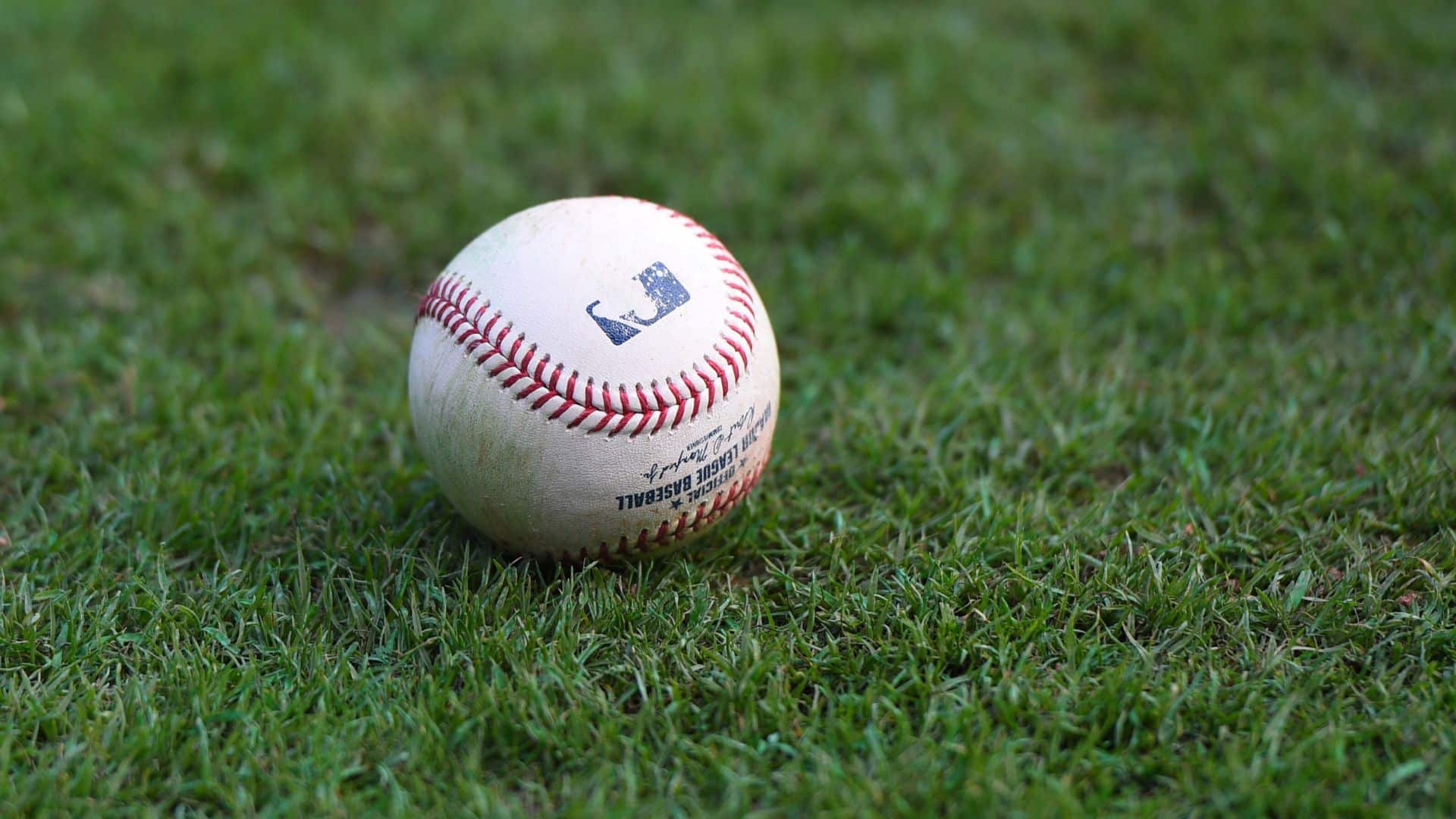 a close up of a worn baseball resting on green grass showing red stitching and scuff marks from repeated use in play