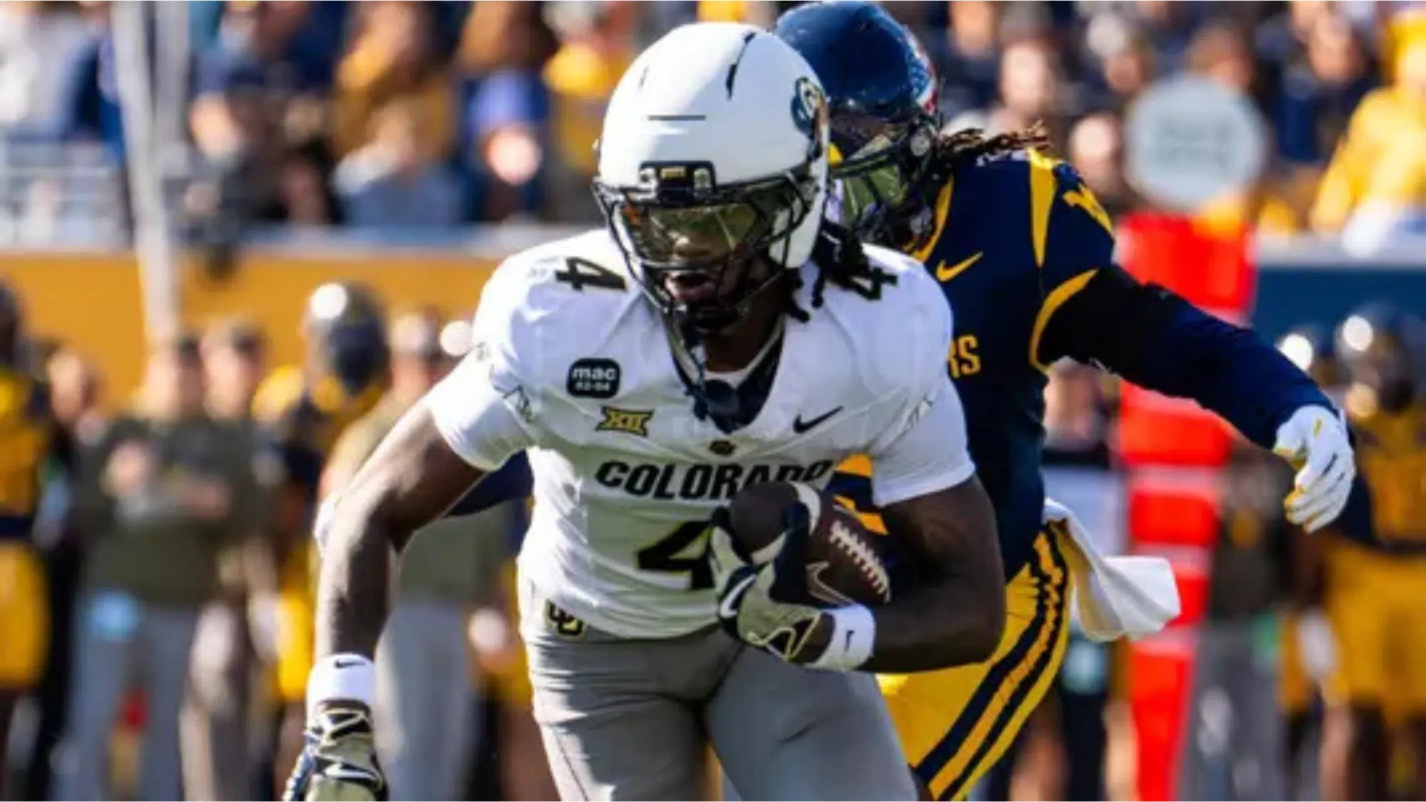 a colorado football player wearing number 4 runs with the ball while a defender in blue and yellow pursues him on the field