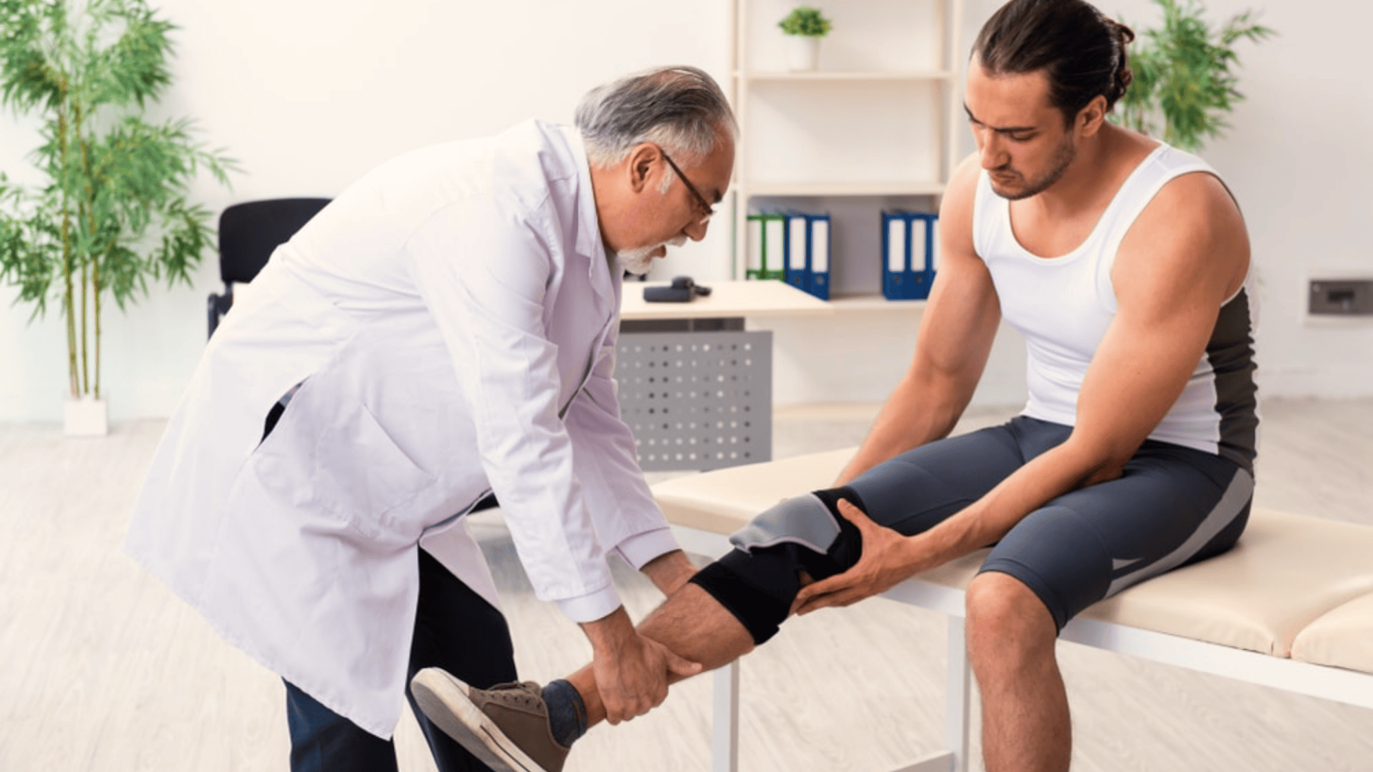 a doctor examines injured knee of a man in a clinic while the patient sits on an exam table wearing athletic clothing