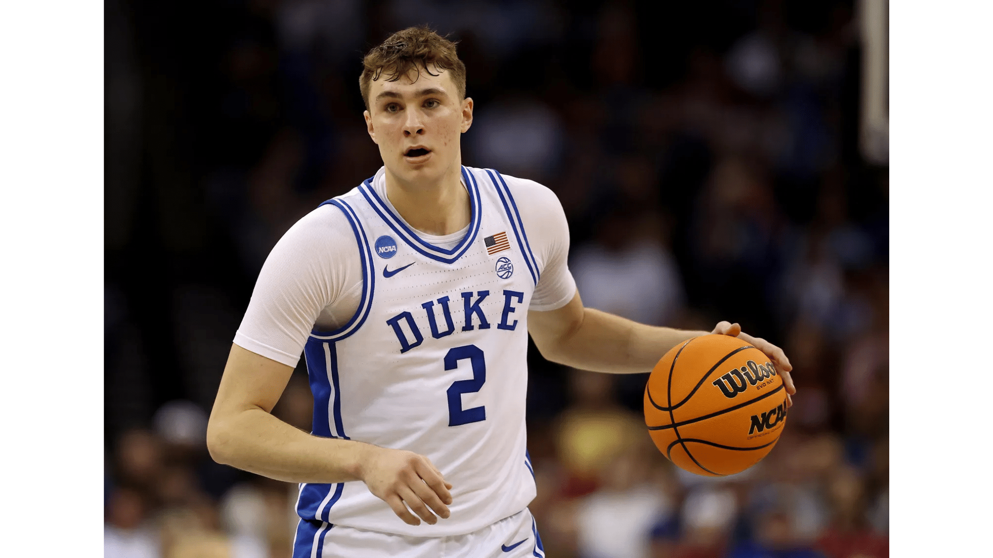 a duke basketball player wearing number 2 dribbles the ball during a game with a blurred crowd in the background