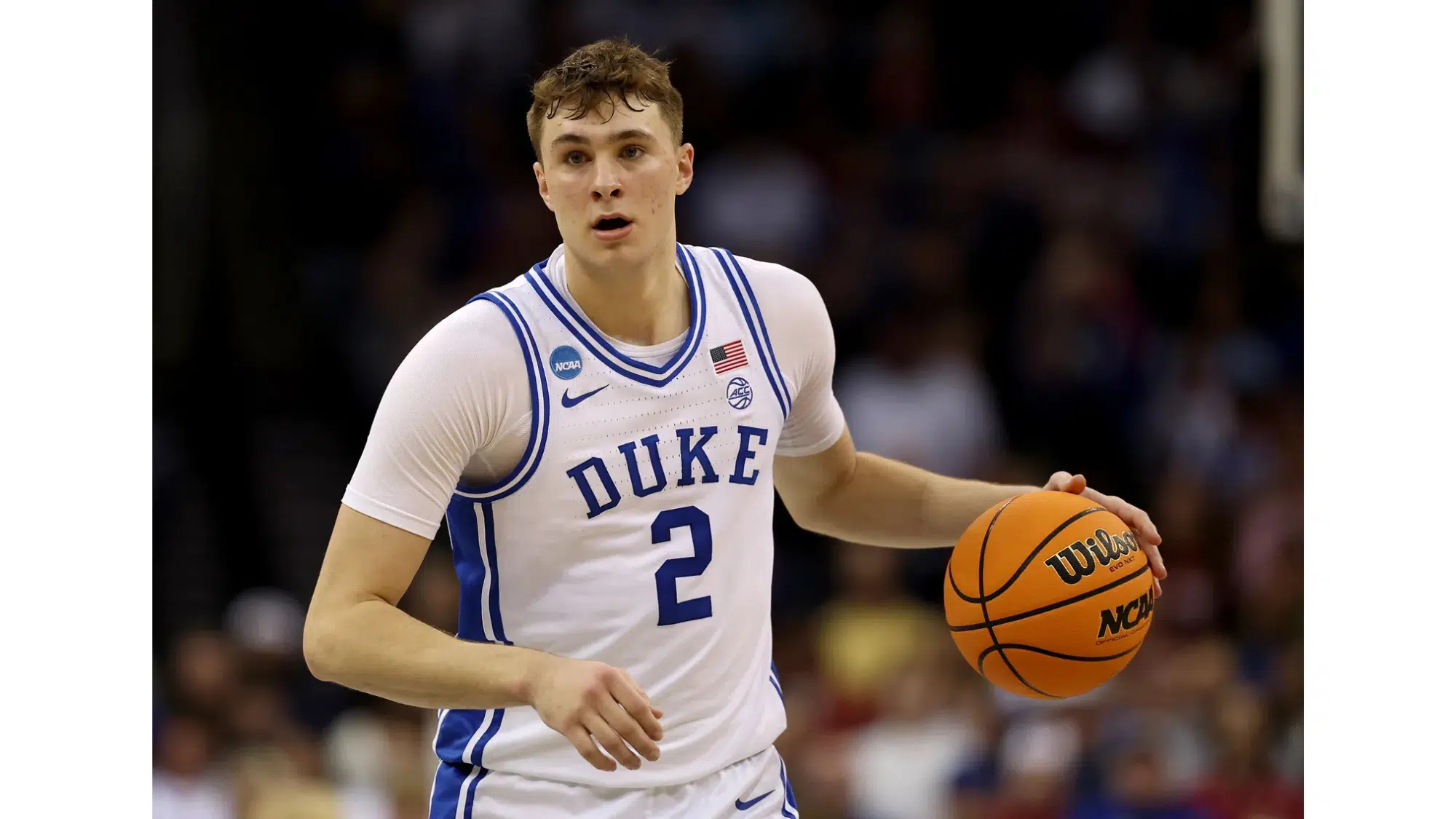 a duke basketball player wearing number 2 dribbles the ball during a game with a blurred crowd in the background