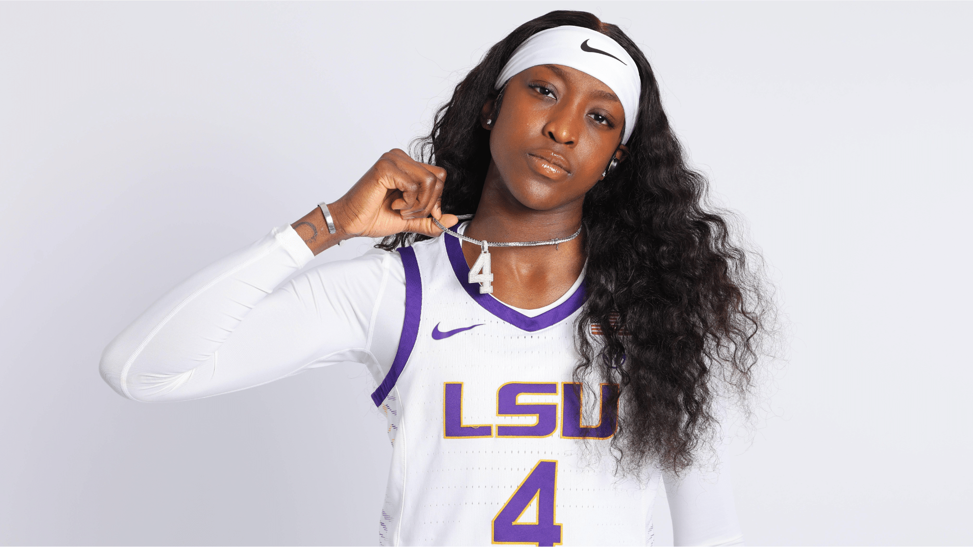 a female LSU basketball player wearing number 4 holds up a necklace while posing against a plain background