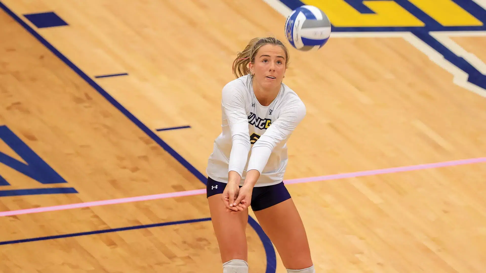 a female volleyball player performing a forearm pass during an indoor volleyball match on a wooden court
