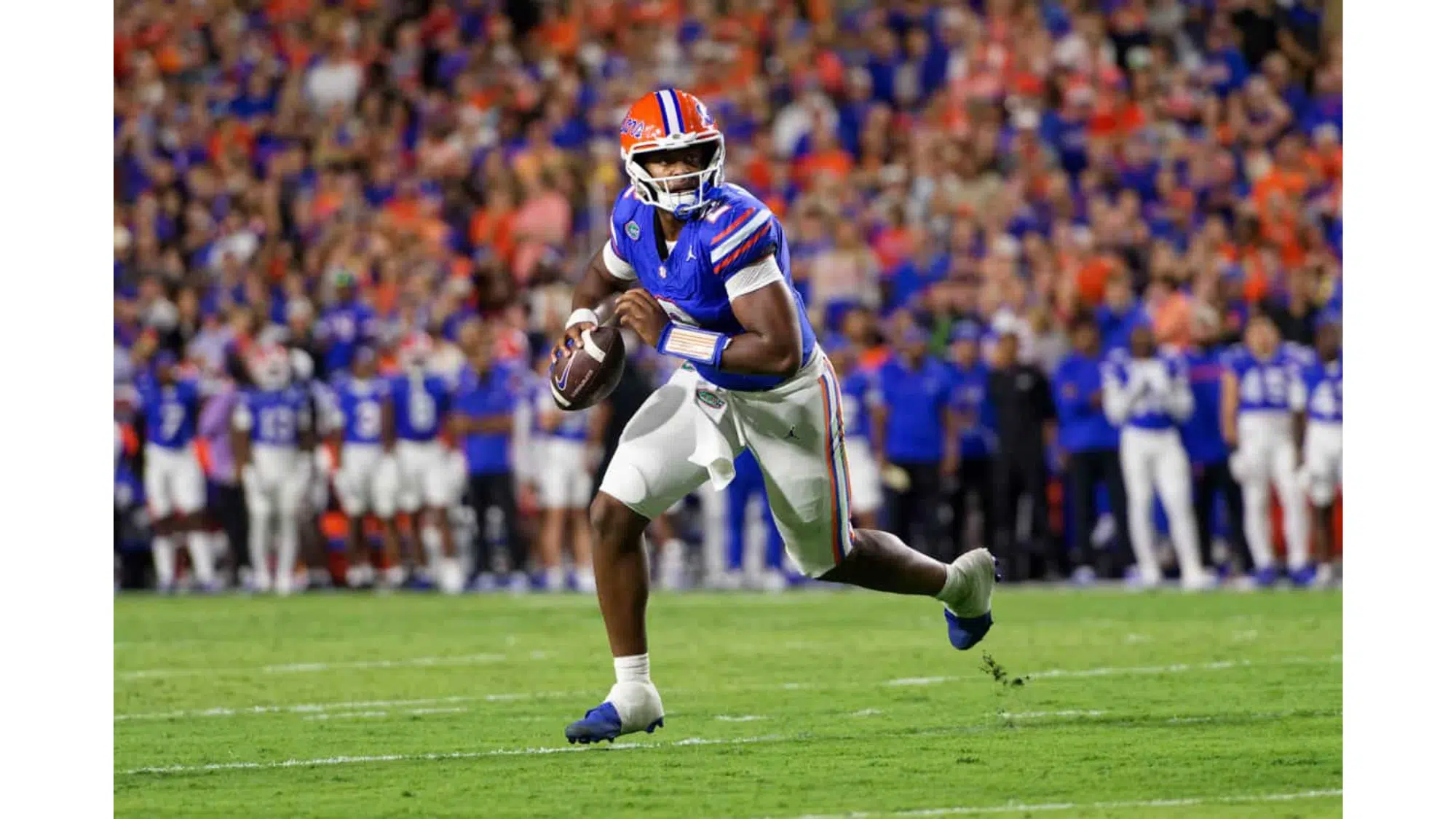 a florida gators football player in a blue jersey runs with the ball during a game with a crowded stadium in the background