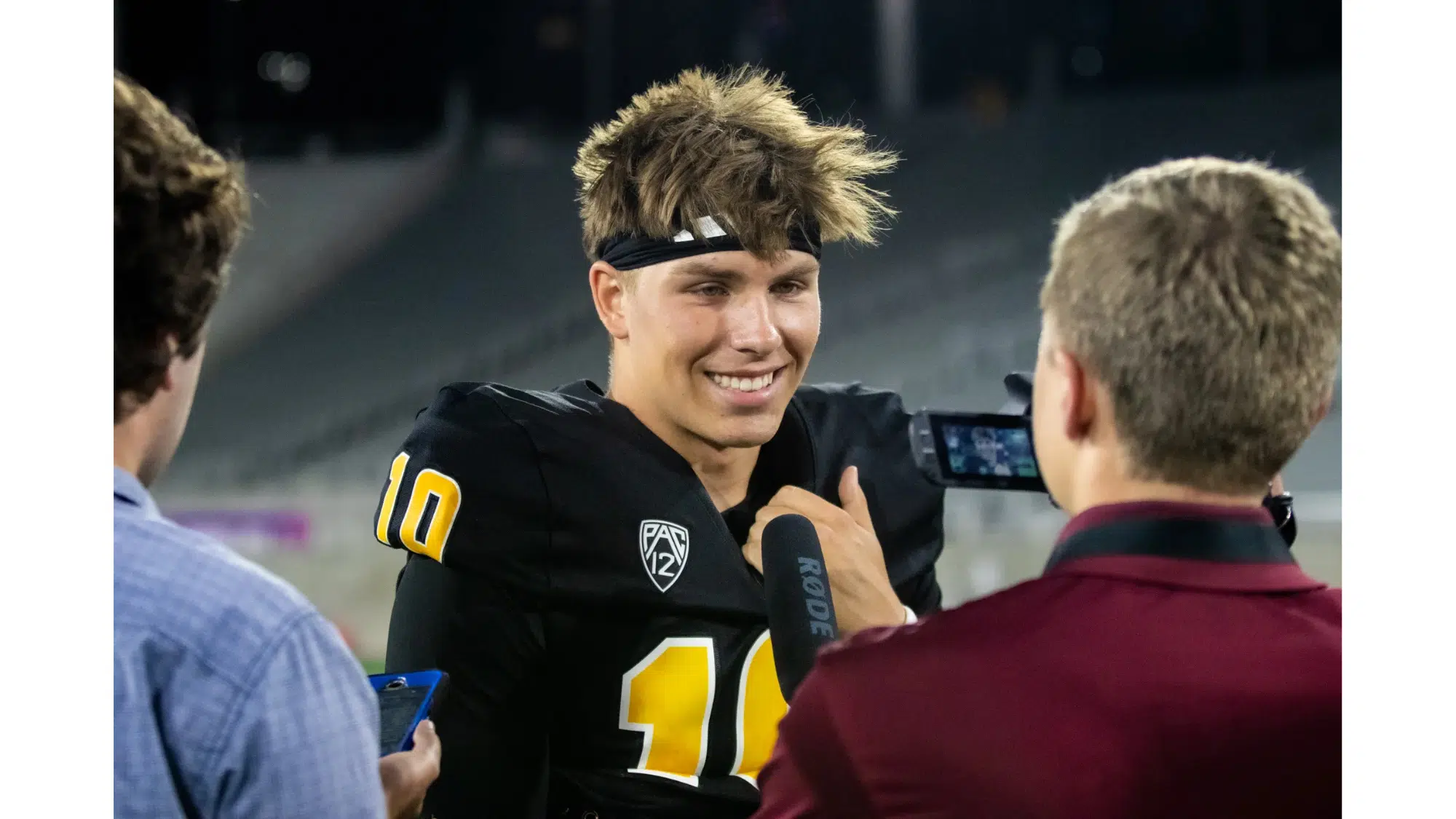 a football player wearing a black jersey with number 10 smiles while being interviewed on the field after a game