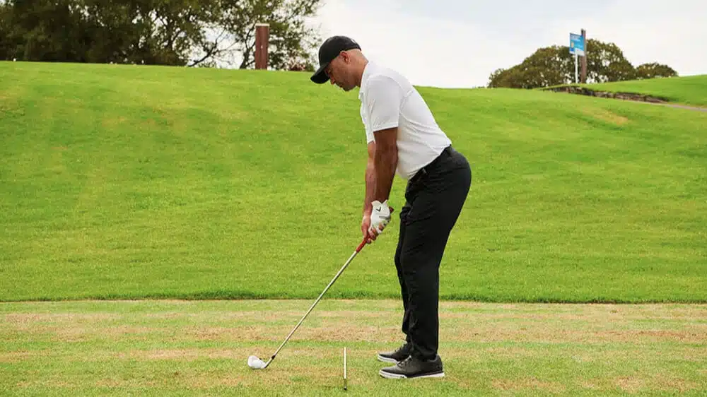 a golfer addresses the ball with an iron on short grass practicing proper stance and posture on a gently sloped fairway