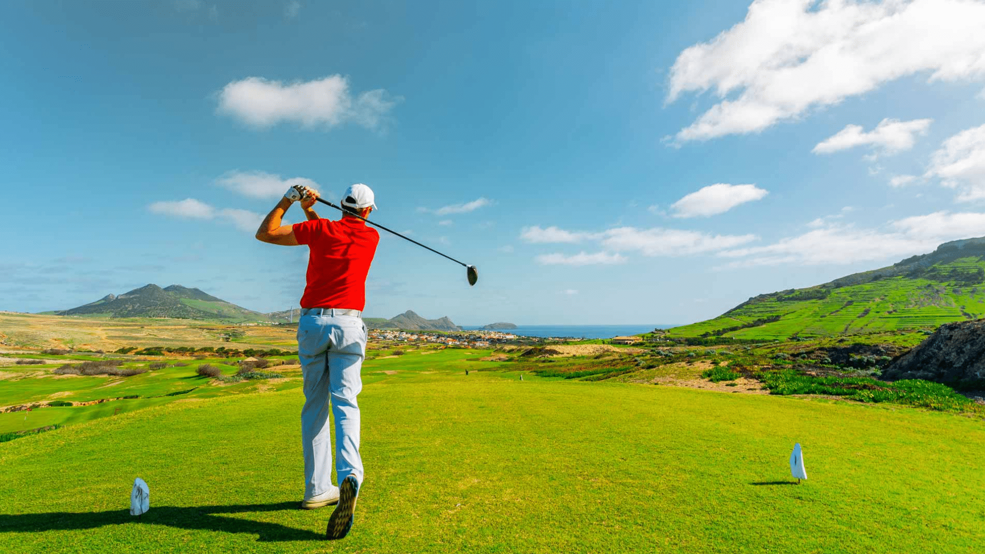 a golfer in a red shirt swinging a driver on a lush coastal course demonstrating powerful golf shots names