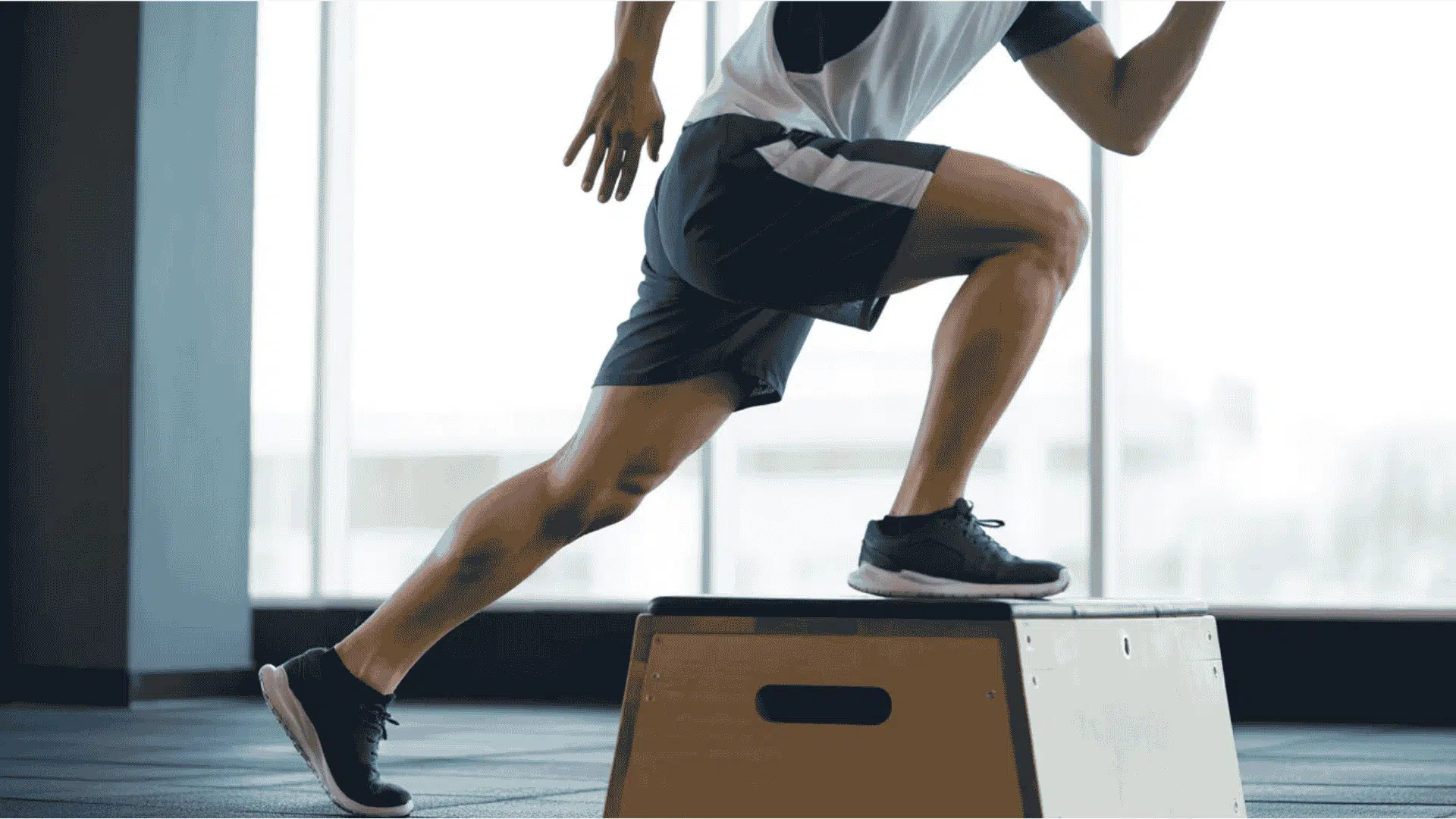 a man performing a step up exercise on a wooden plyo box in a bright gym setting