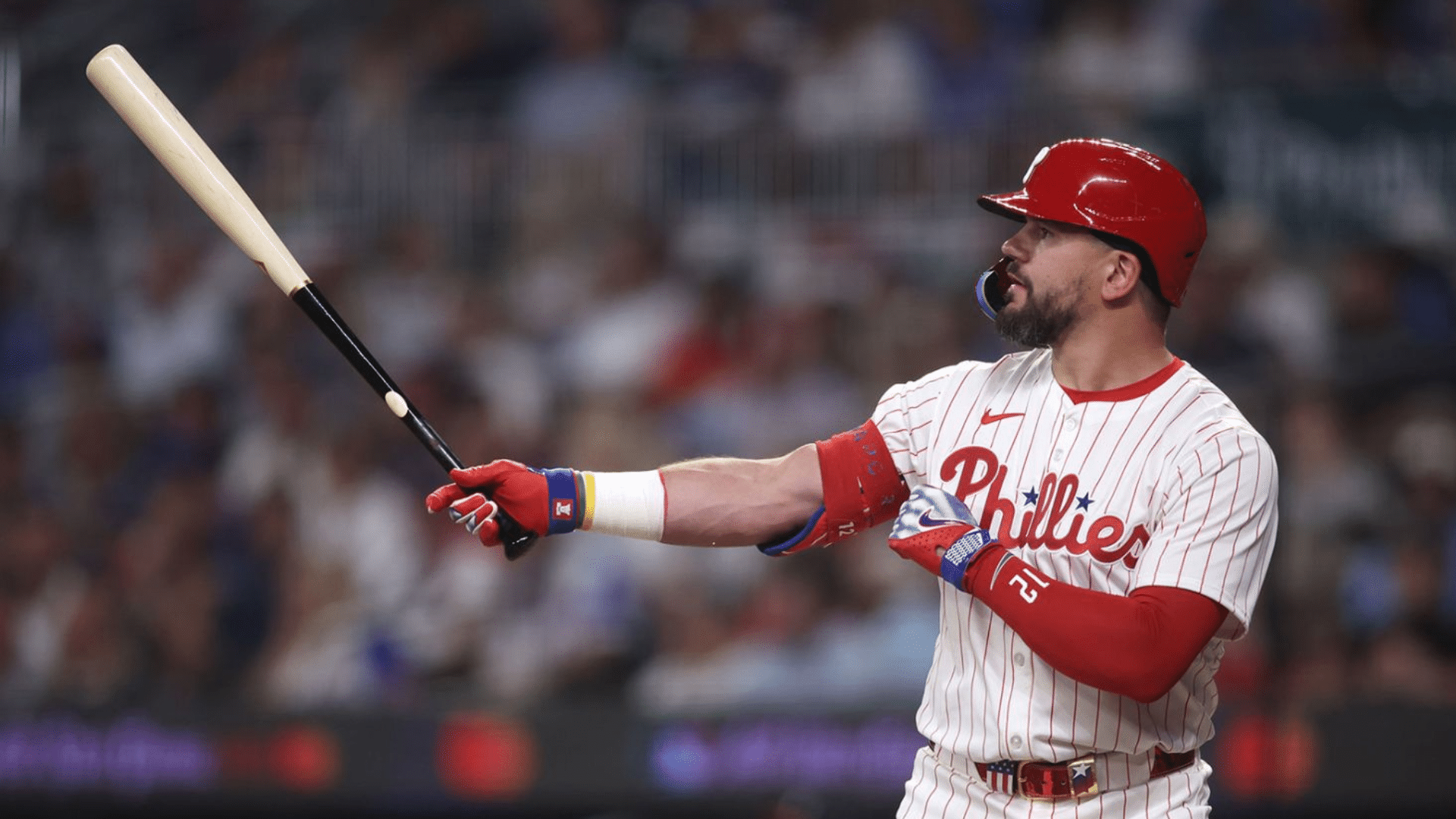 a philadelphia phillies baseball player in a red helmet follows through on a powerful swing during a major league game at bat