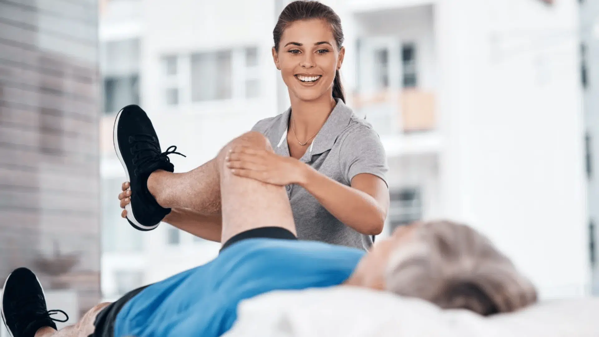 a physical therapist assisting a patient lying on a table to evaluate passive range of motion in the knee during rehabilitation
