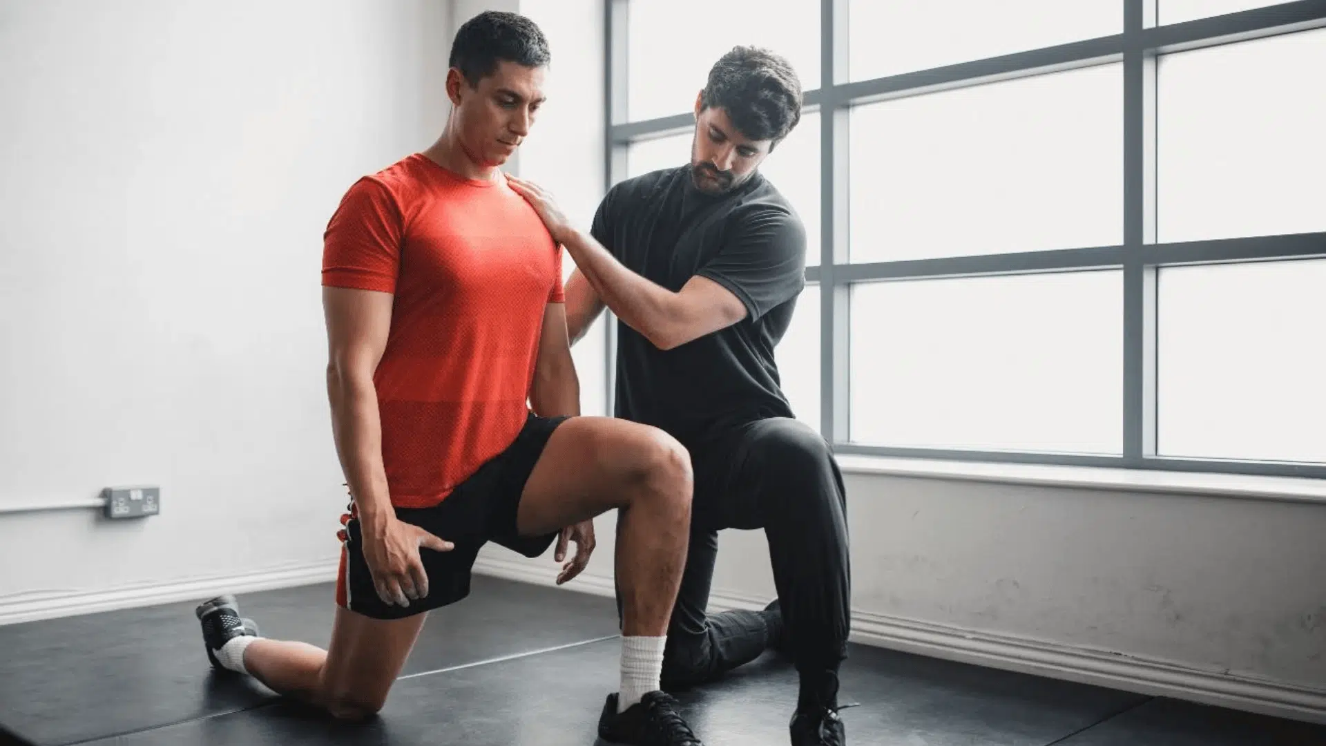 a physical therapist guiding a man through a kneeling lunge to assess passive range of motion in a clinic