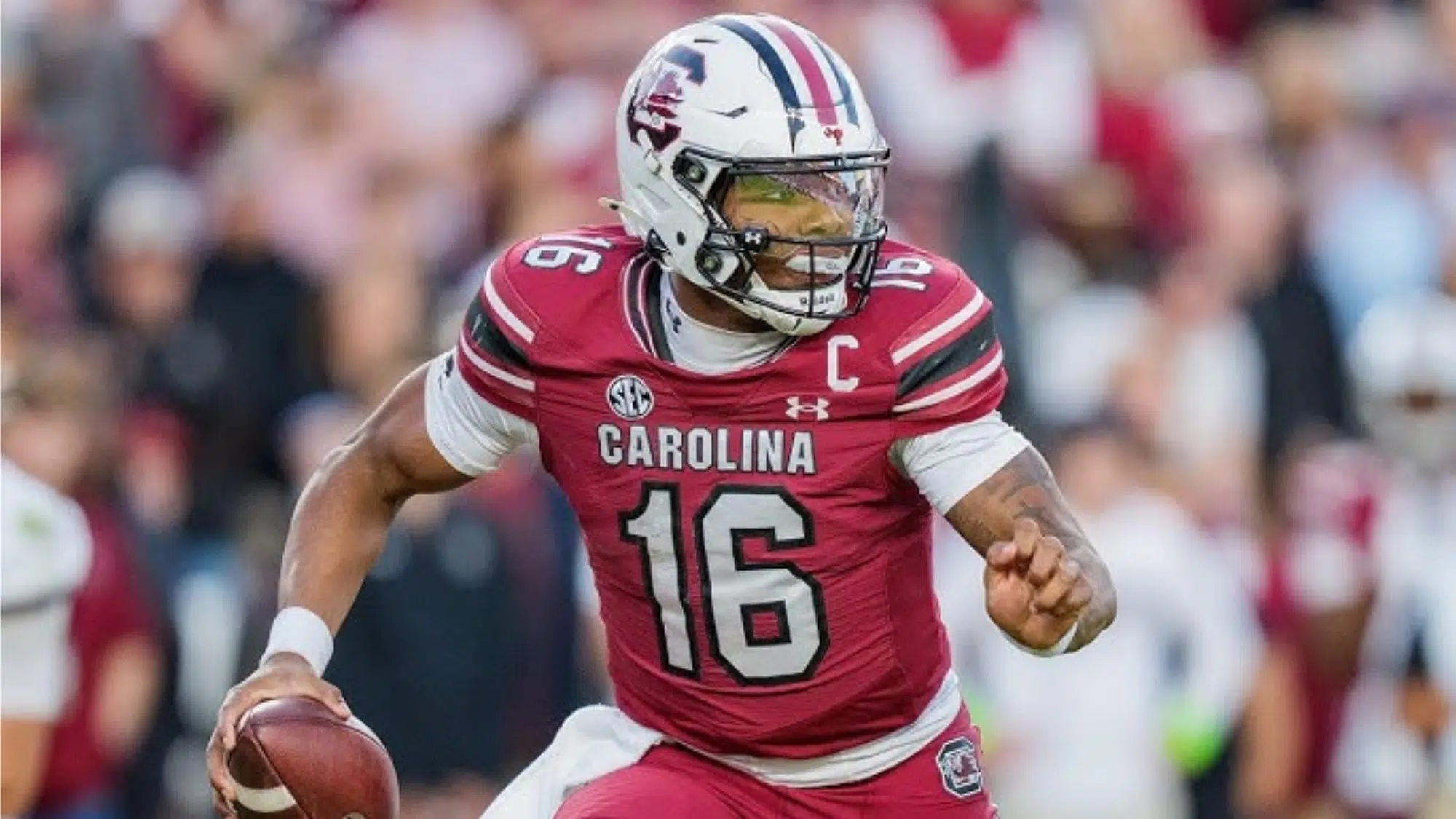 a south carolina nil earner football player wearing number 16 runs with the ball during a game with a blurred crowd in the background
