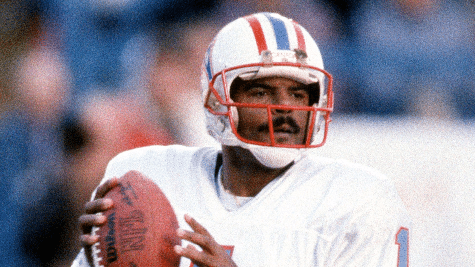a vintageera quarterback holds the football, scanning the field during a play.
