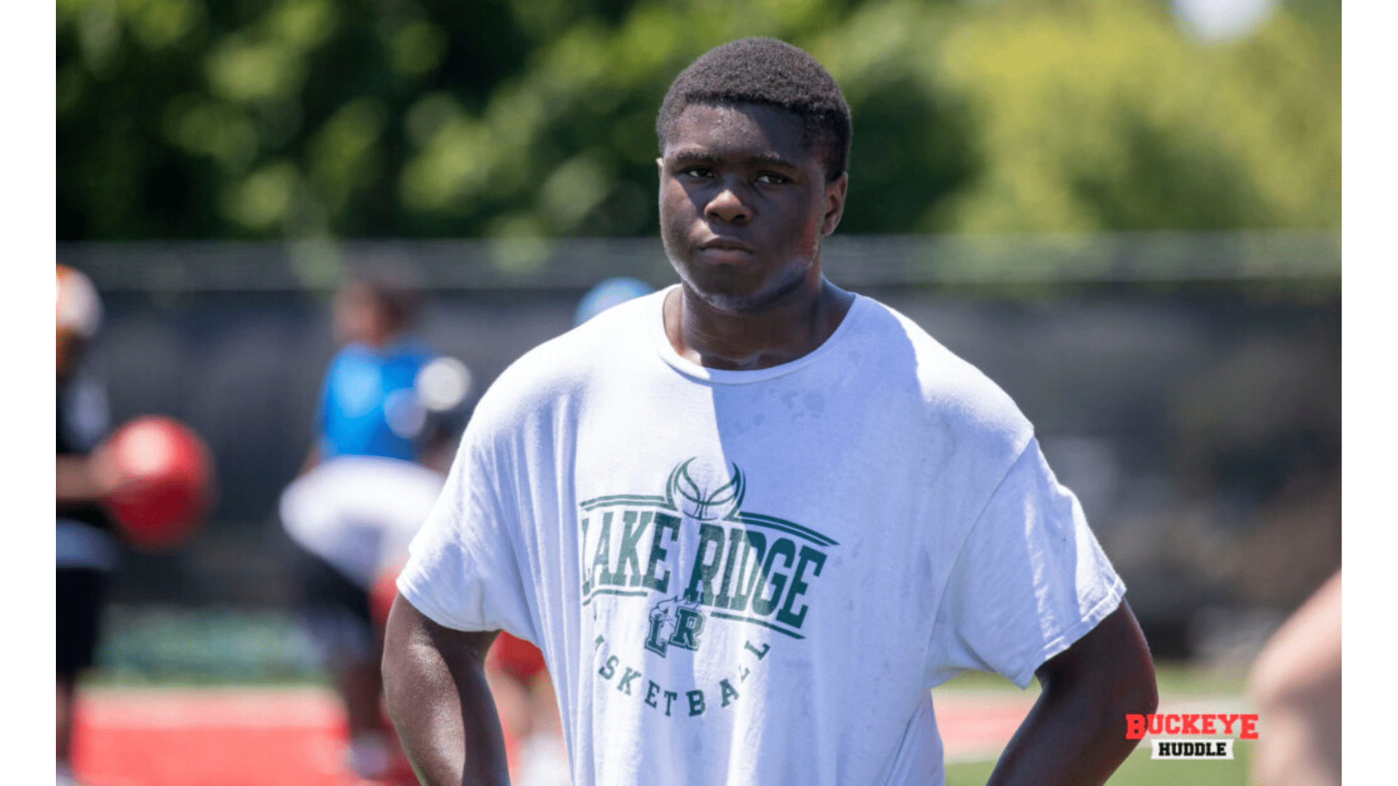 a young top nil earners wearing a white lake ridge Basketball t shirt stands on an outdoor field during practice with hands on hips