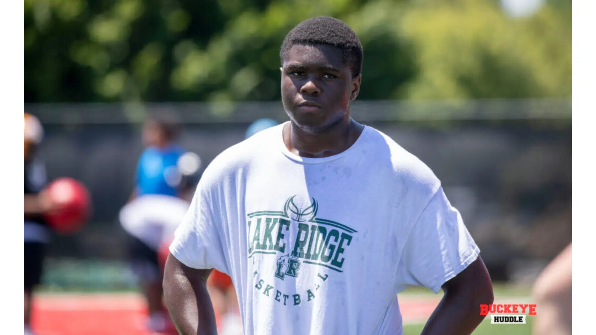 a young top nil earners wearing a white lake ridge Basketball t shirt stands on an outdoor field during practice with hands on hips