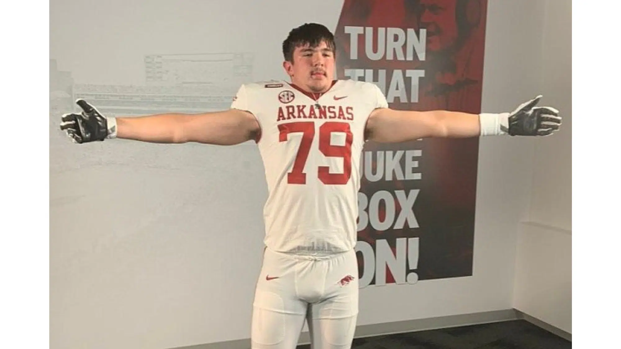 an arkansas football top nil earners wearing number 79 stands with arms outstretched during a team media session indoors