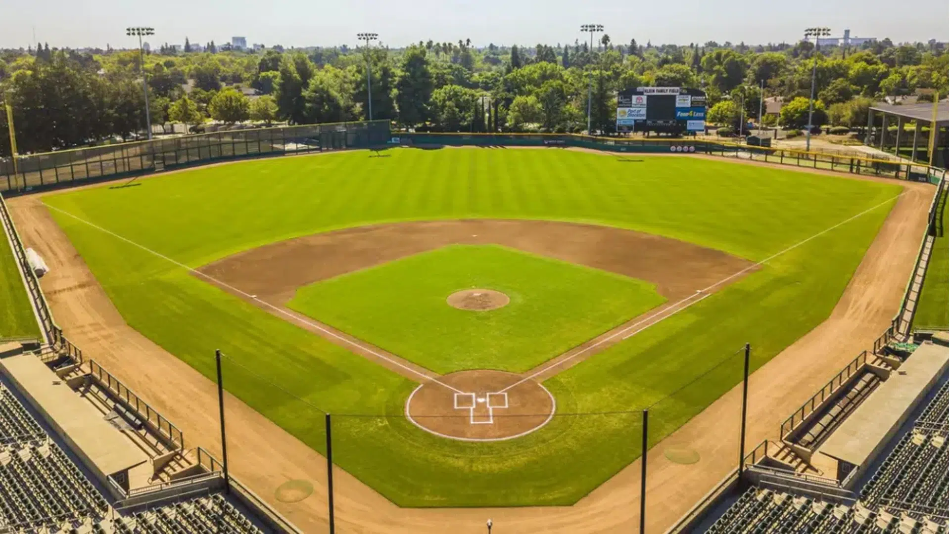 an empty baseball field viewed from behind home plate with green outfield grass dirt infield and stadium seating under a clear sky