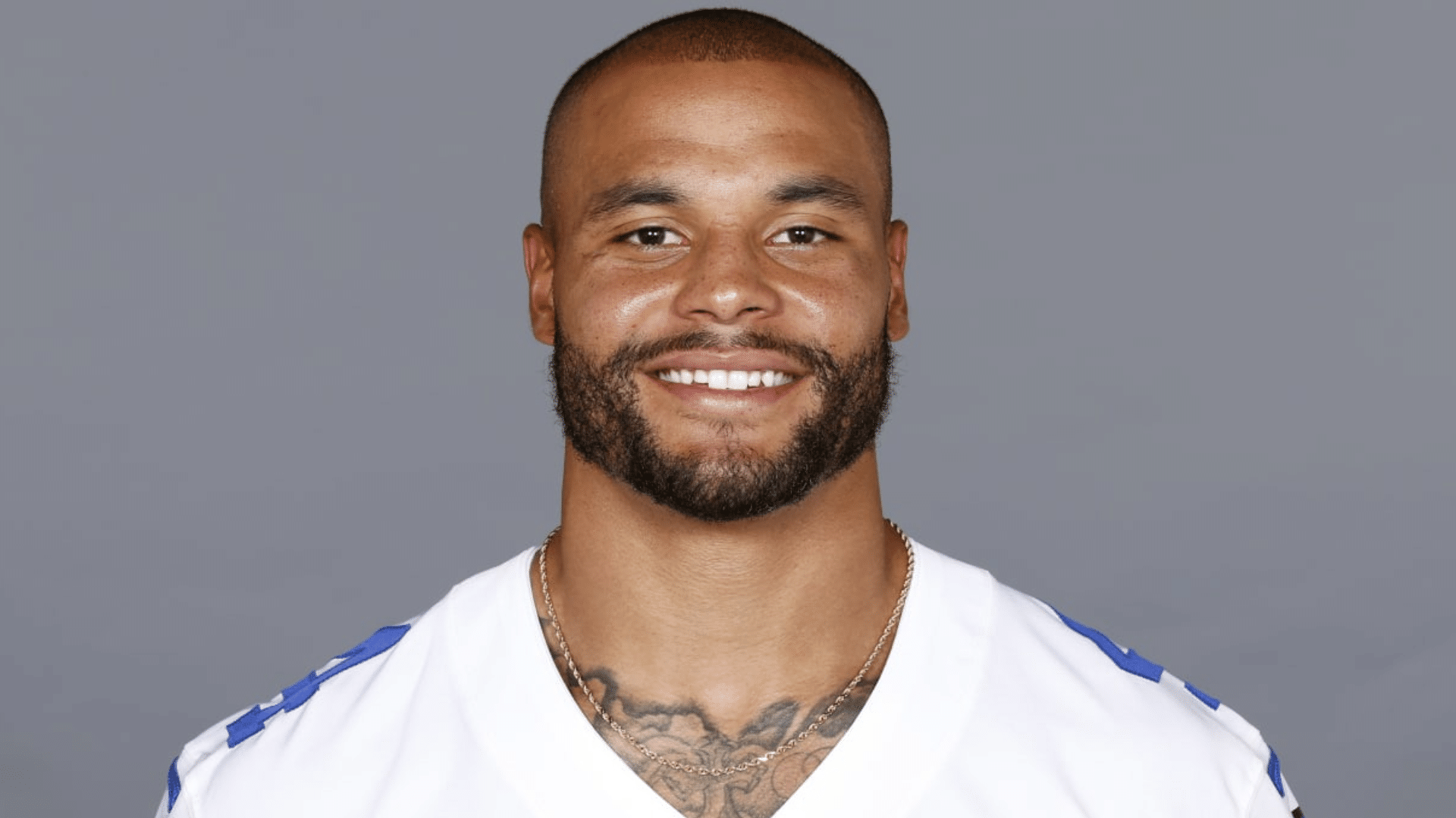 dak prescott smiling poses in a white jersey against a plain background