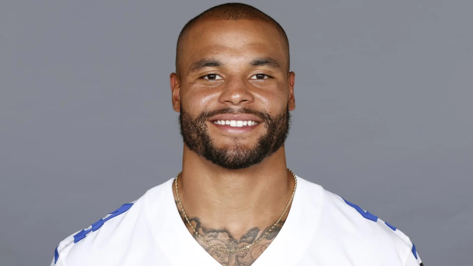 dak prescott smiling poses in a white jersey against a plain background