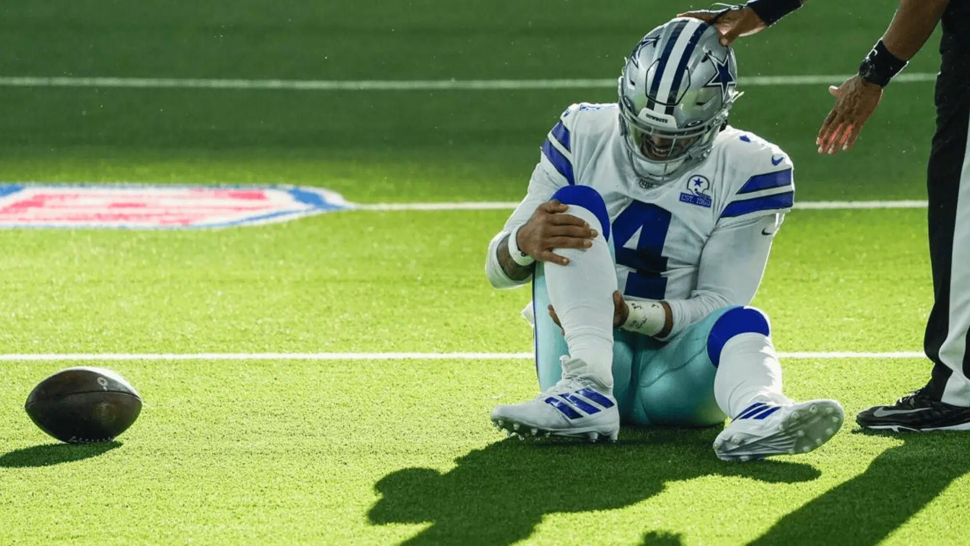 dallas cowboys quarterback dak prescott sitting on the field holding his knee as a staff member reaches out