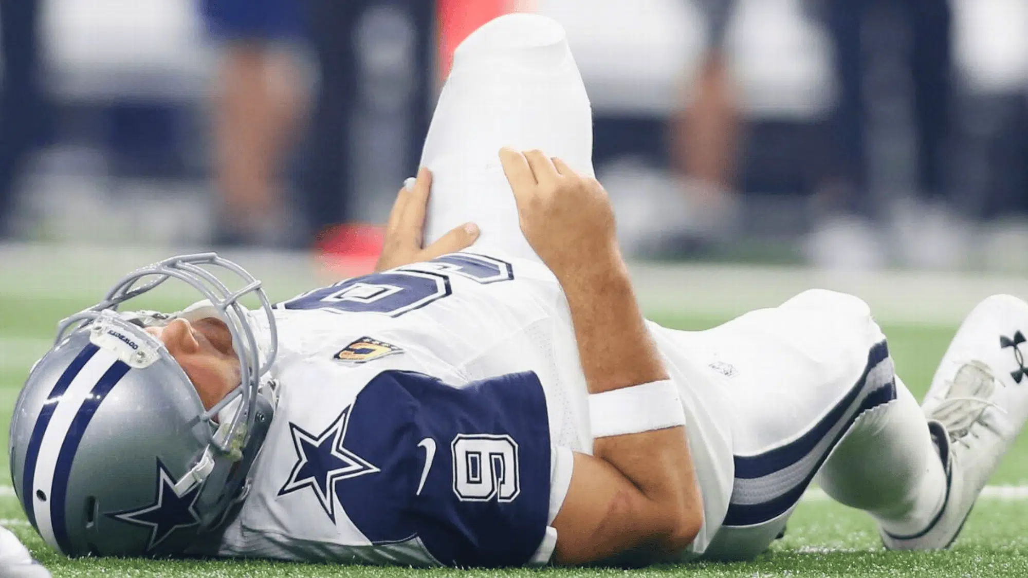 dallas cowboys quarterback tony romo lying on the field holding his leg after an apparent injury