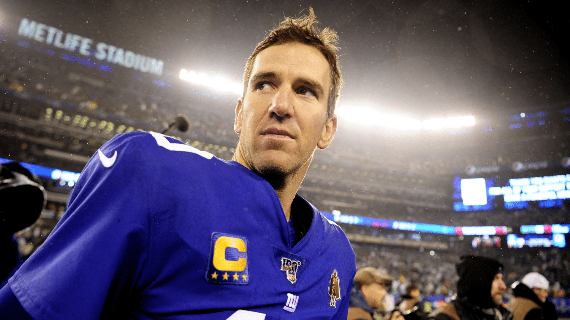 eli manning football player in a blue jersey looks on under bright stadium lights after a game