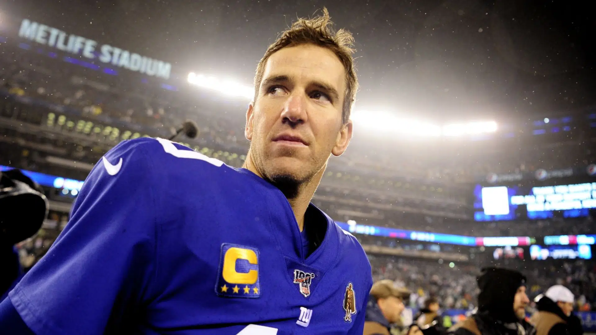 eli manning football player in a blue jersey looks on under bright stadium lights after a game