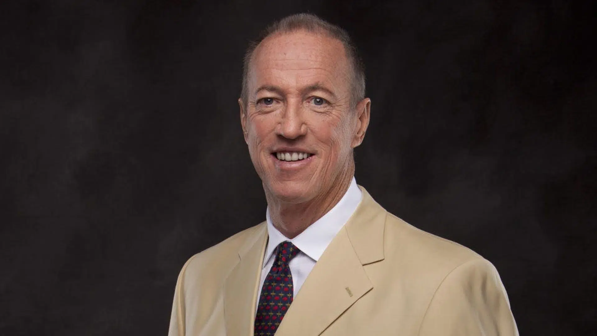 jim kelly smiling man in a light coloured suit poses against a dark background