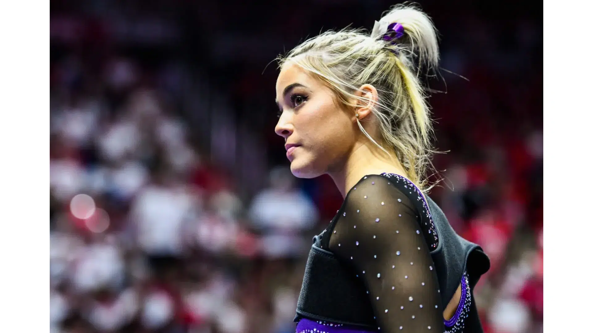 livvy dunne a gymnast in a purple and black leotard with sheer sleeves looking focused in a crowded arena