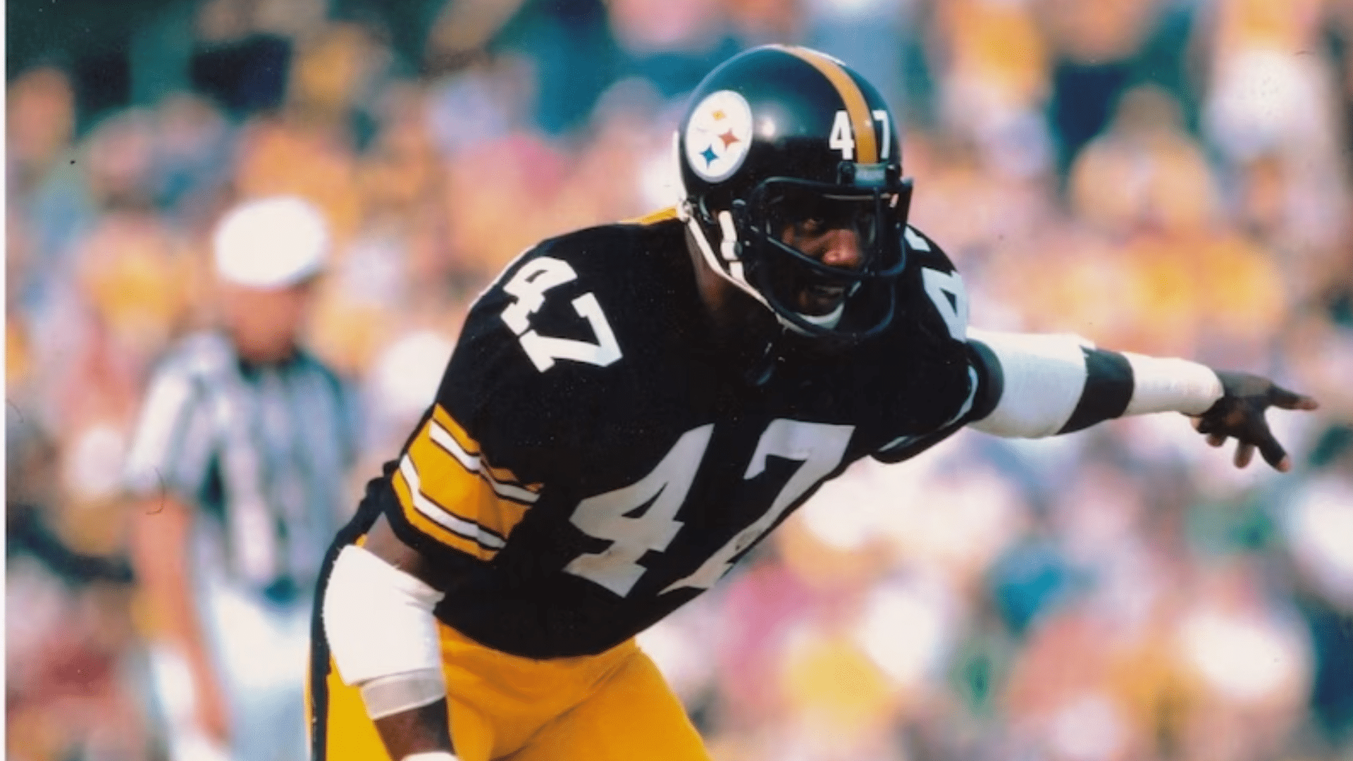mel blount in a black and yellow uniform pointing forward on the field during a game with a blurred crowd in background