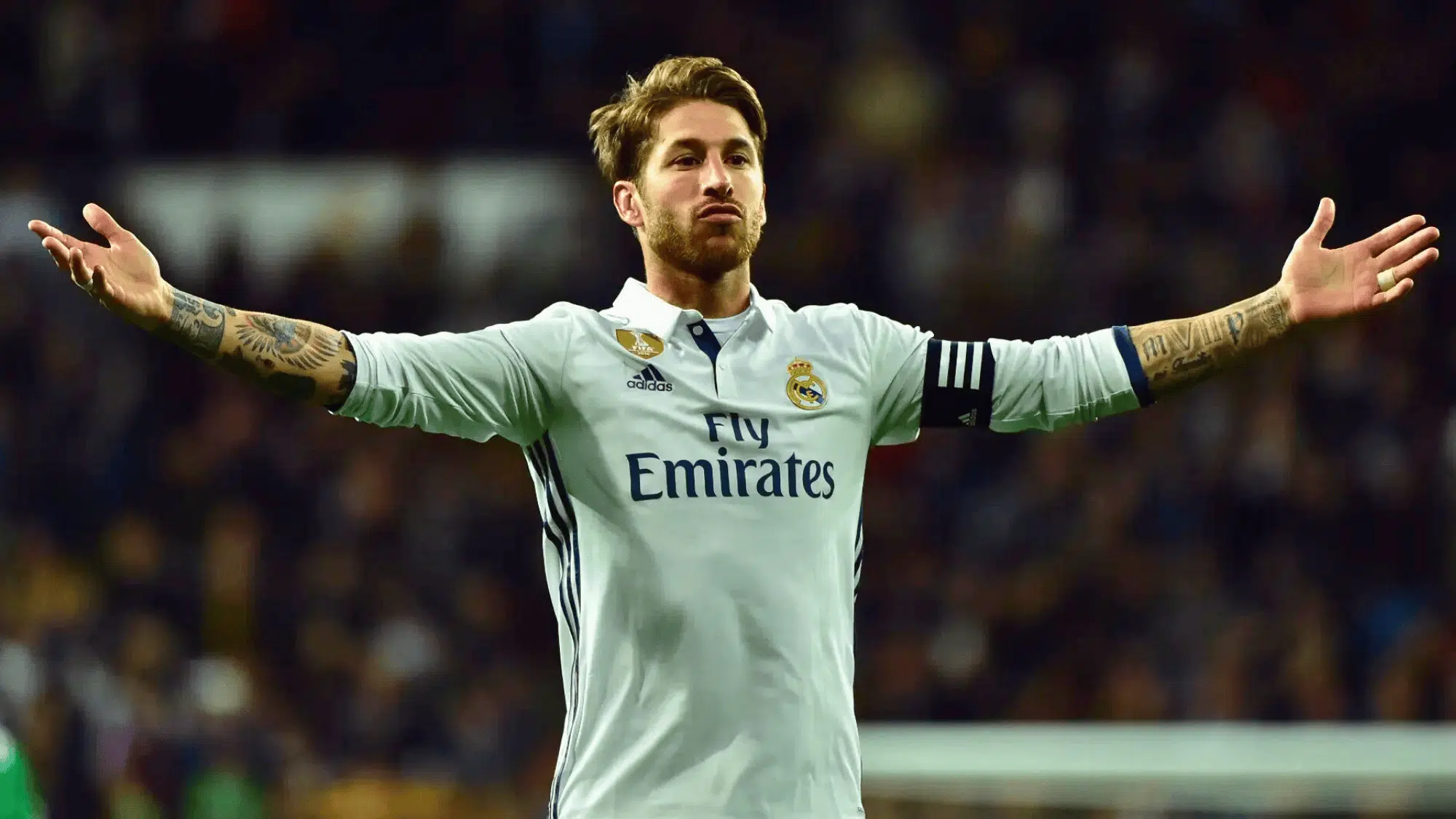 sergio ramos in a white real madrid jersey with arms outstretched on the field