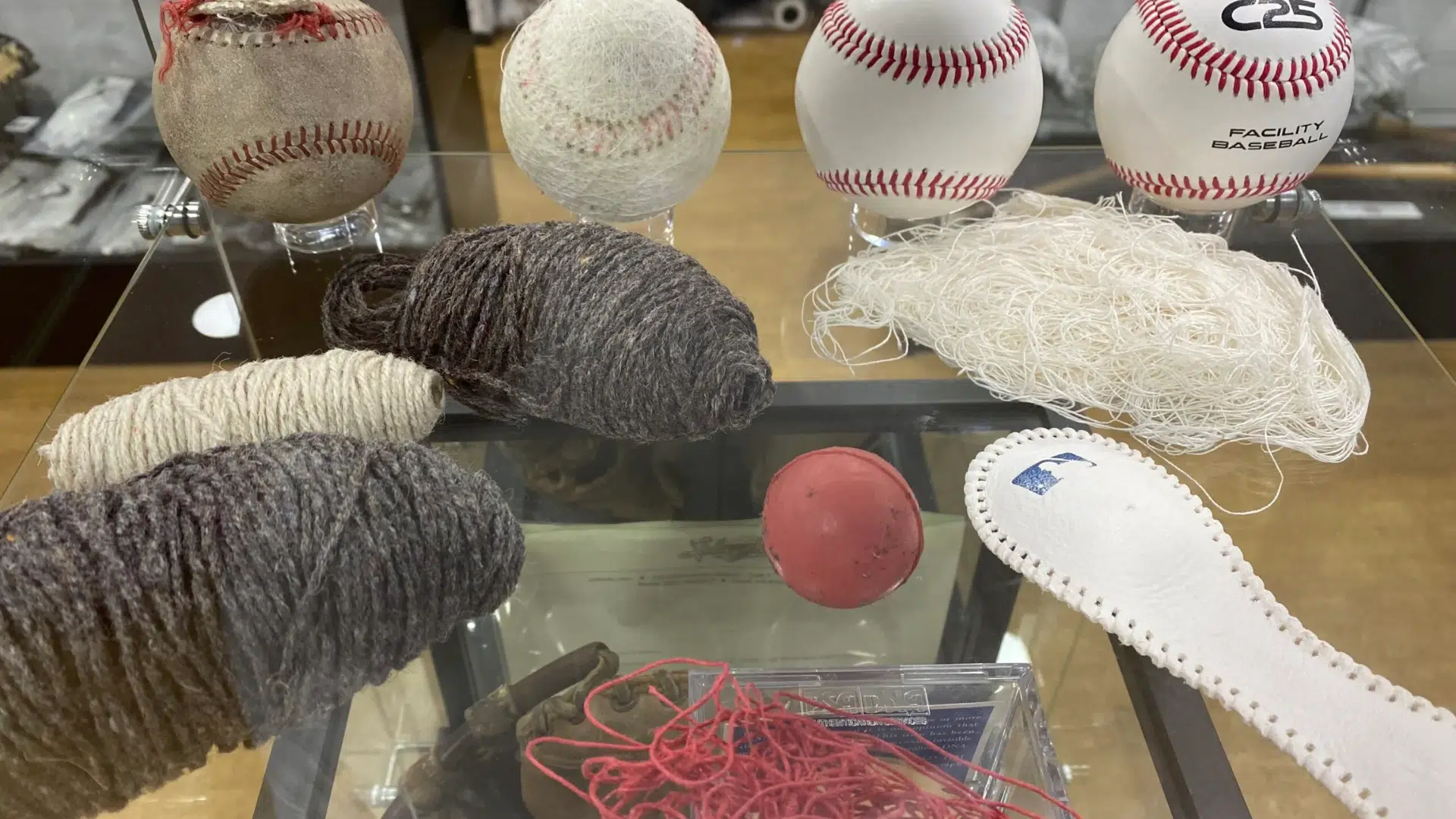 several baseballs showing different construction stages are displayed in a glass case with loose yarn and leather pieces