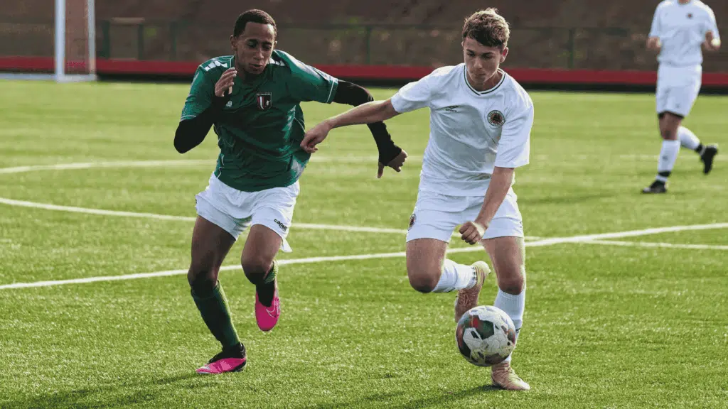 two football players run side by side chasing the football in an intense match