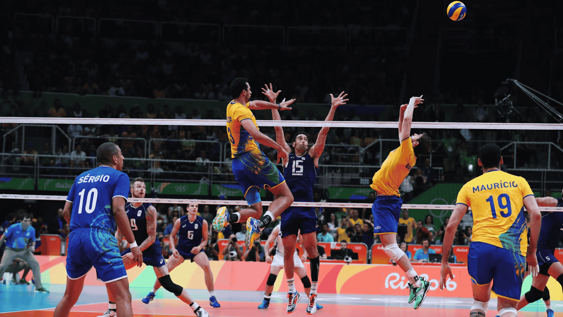 volleyball players leap at the net as volleyball arcs overhead during an intense volleyball match in a packed arena