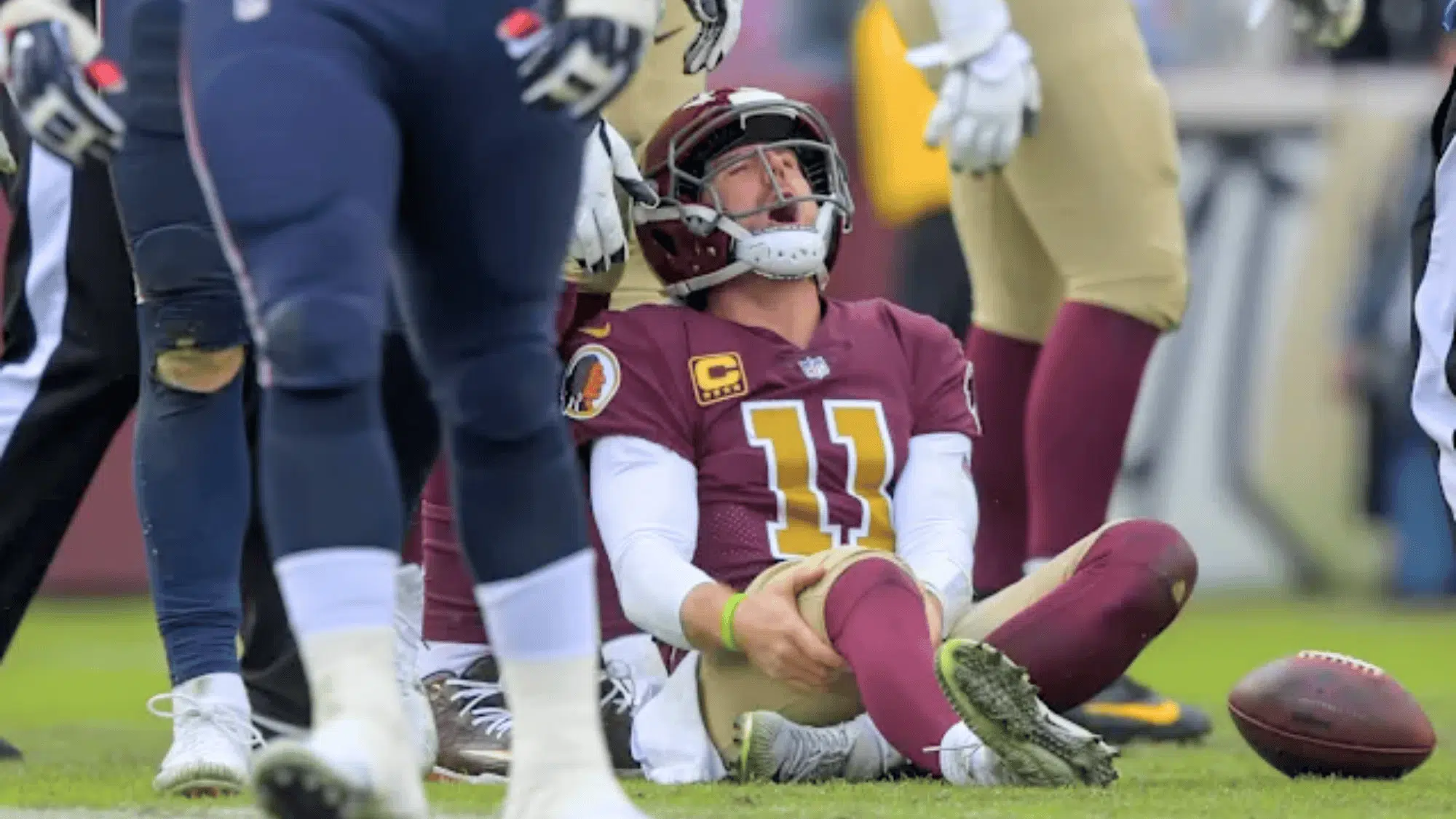 washington player alex smith sitting on the field holding his knee in pain after a tackle