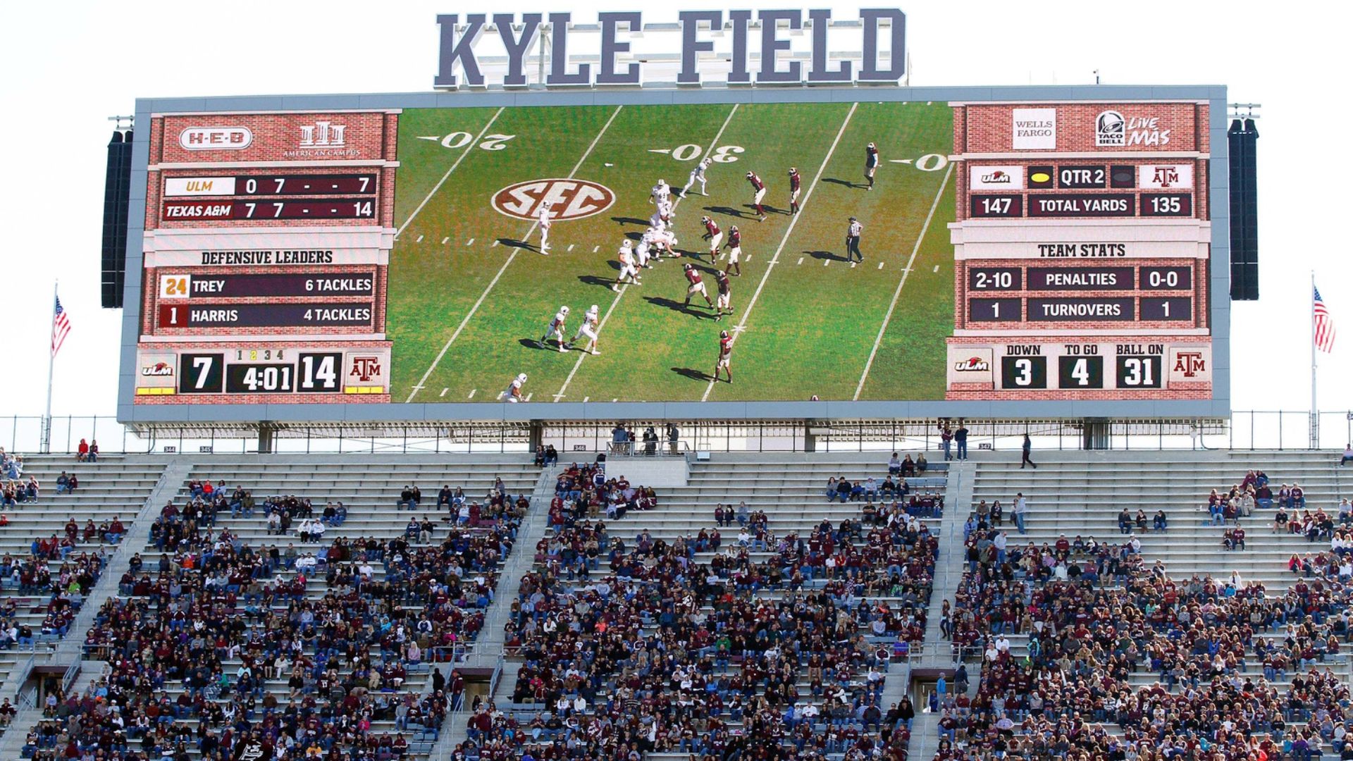 A large stadium video scoreboard at Kyle Field shows a college football game while fans fill the stands below