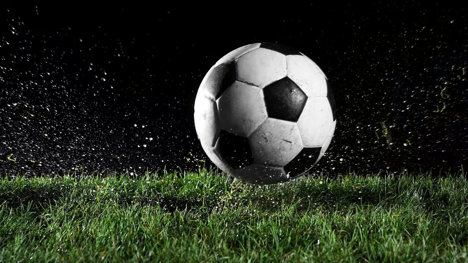 a black and white soccer ball bouncing on green grass with water droplets splashing against a dark background