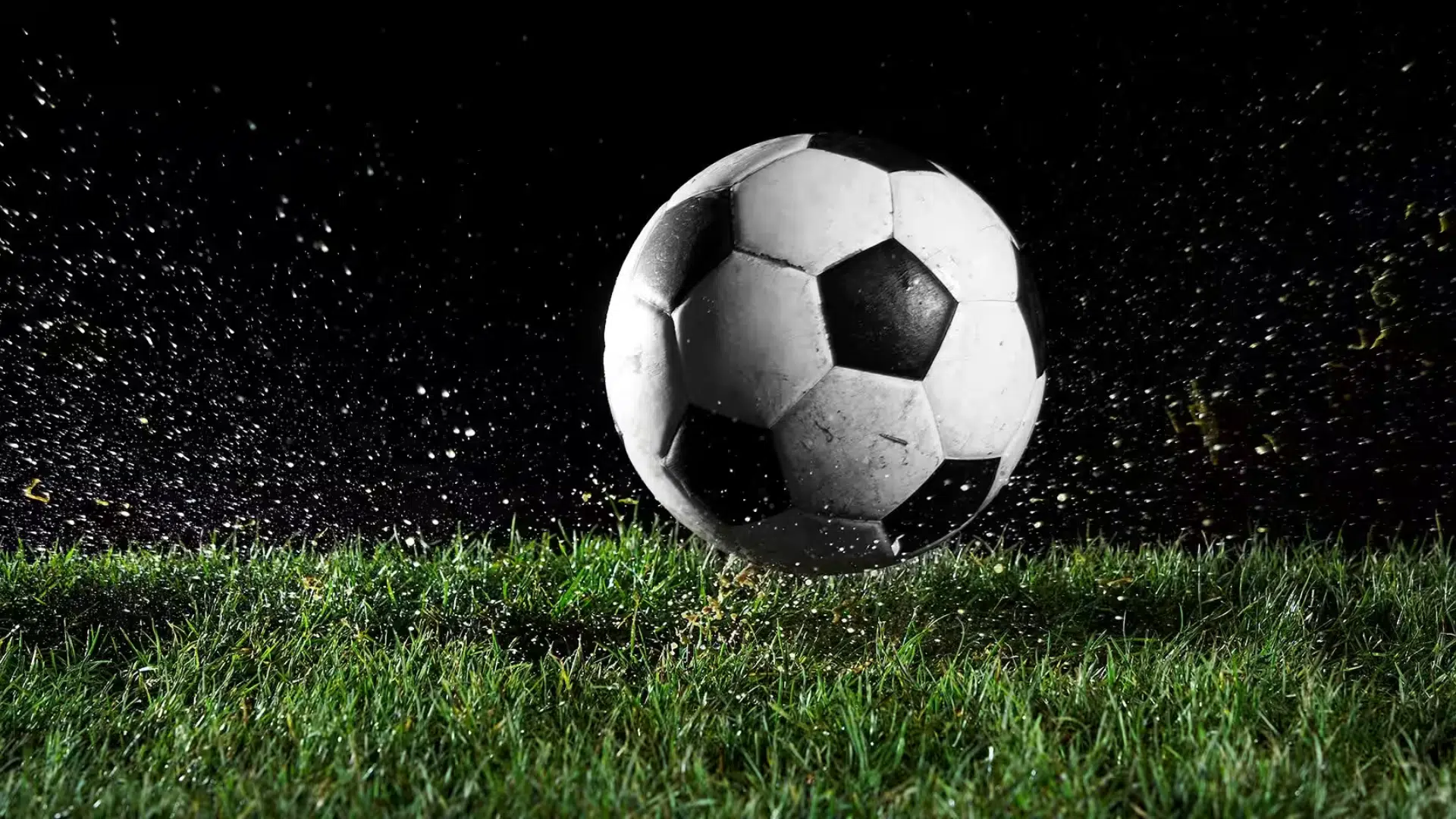 a black and white soccer ball bouncing on green grass with water droplets splashing against a dark background
