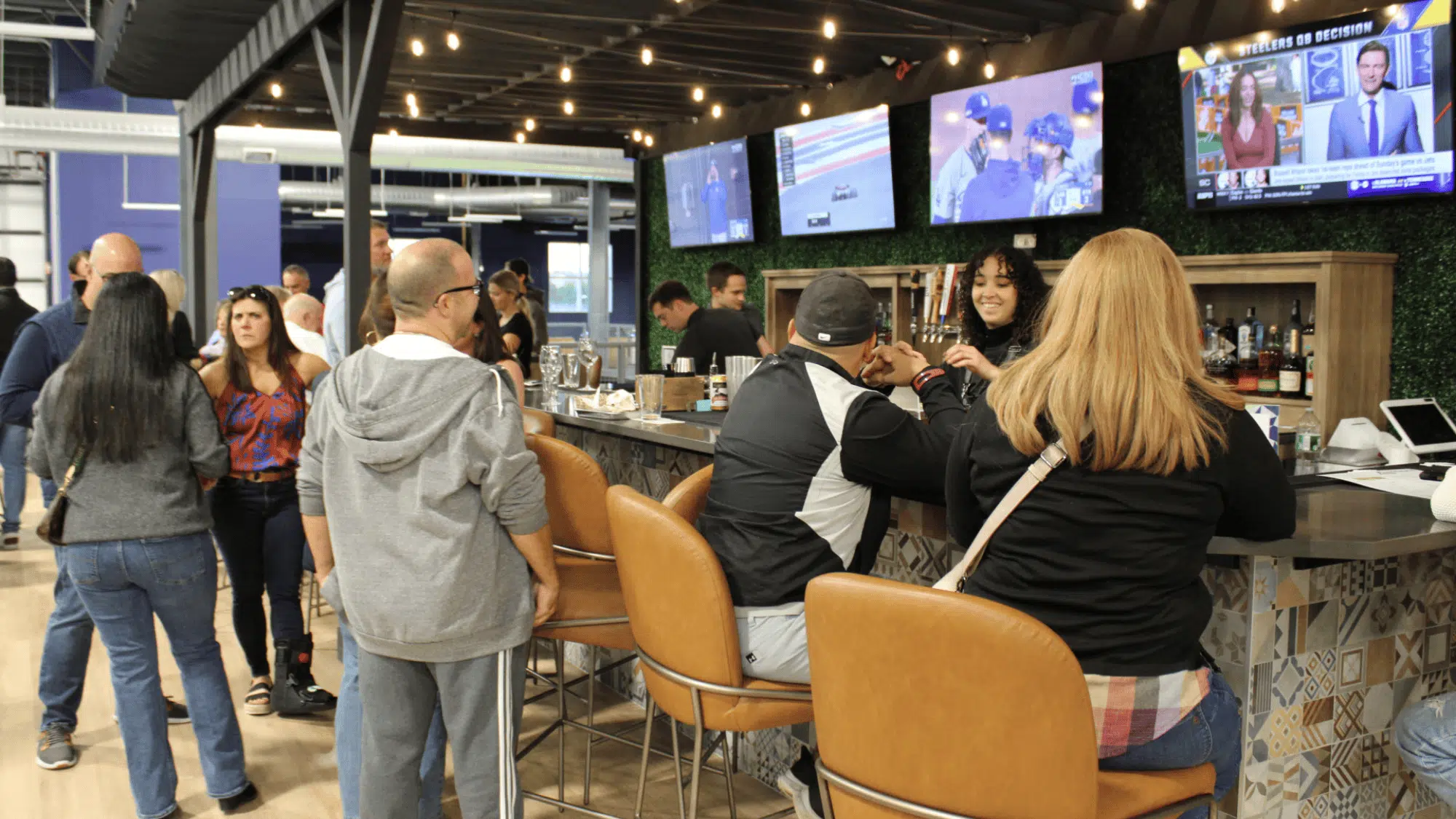a lively bar scene with people socializing, sitting on tan stools at a counter