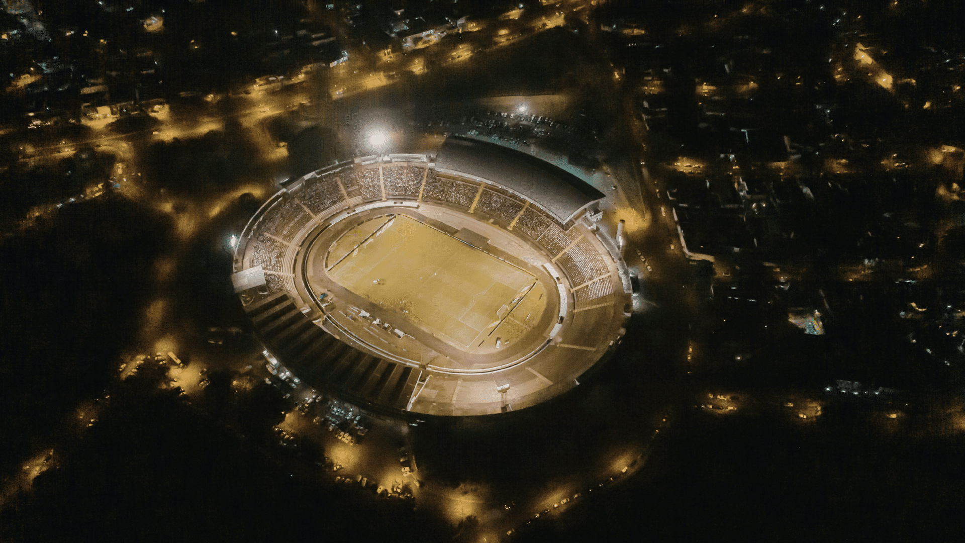 aerial view of a brightly lit stadium at night surrounded by city streets and buildings stadium with 200000 seats history myths records