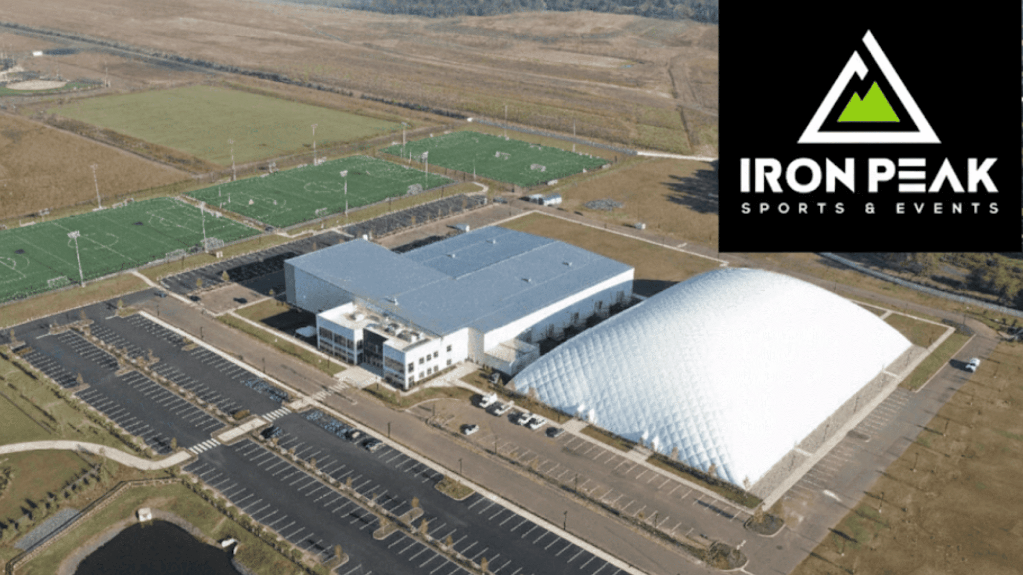 aerial view of iron peak sports & events complex featuring a large building sports dome and adjacent sports fields with vast parking areas