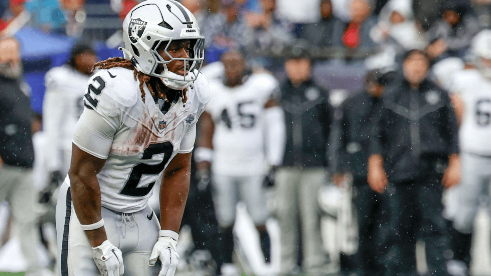 ashton jeanty in a white and silver uniform stands on a rainy field, focused and poised